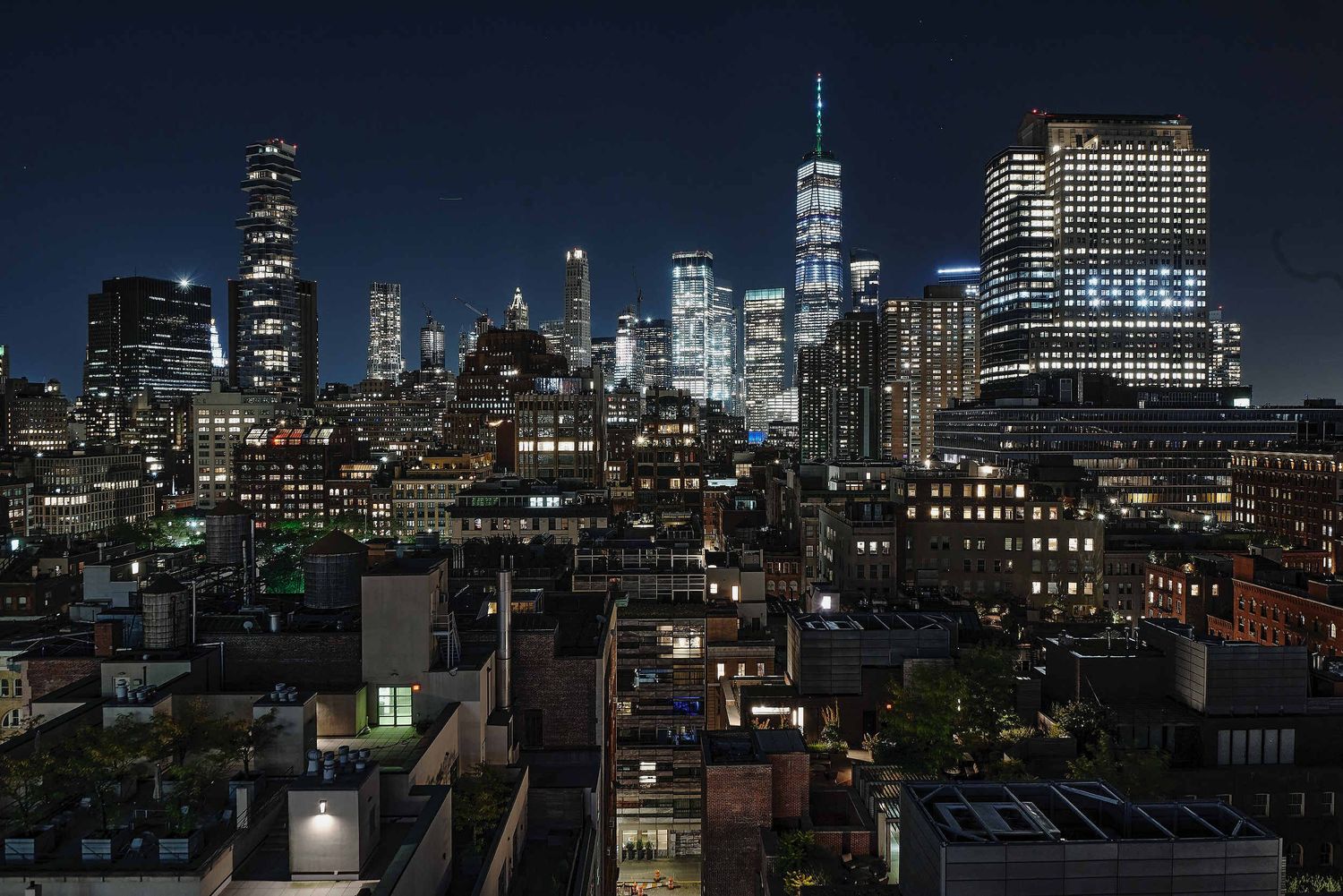 Manhattan skyline at night with illuminated skyscrapers including One World Trade Center rising above city rooftops.