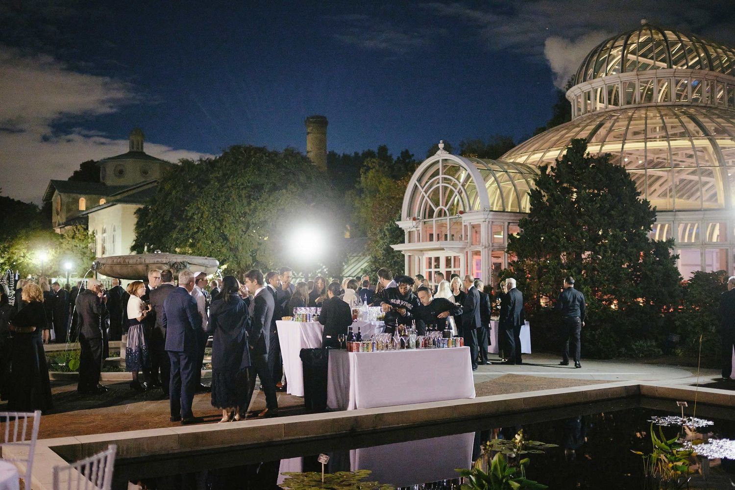 Evening wedding reception gathering outside a grand conservatory building with illuminated dome structure.
