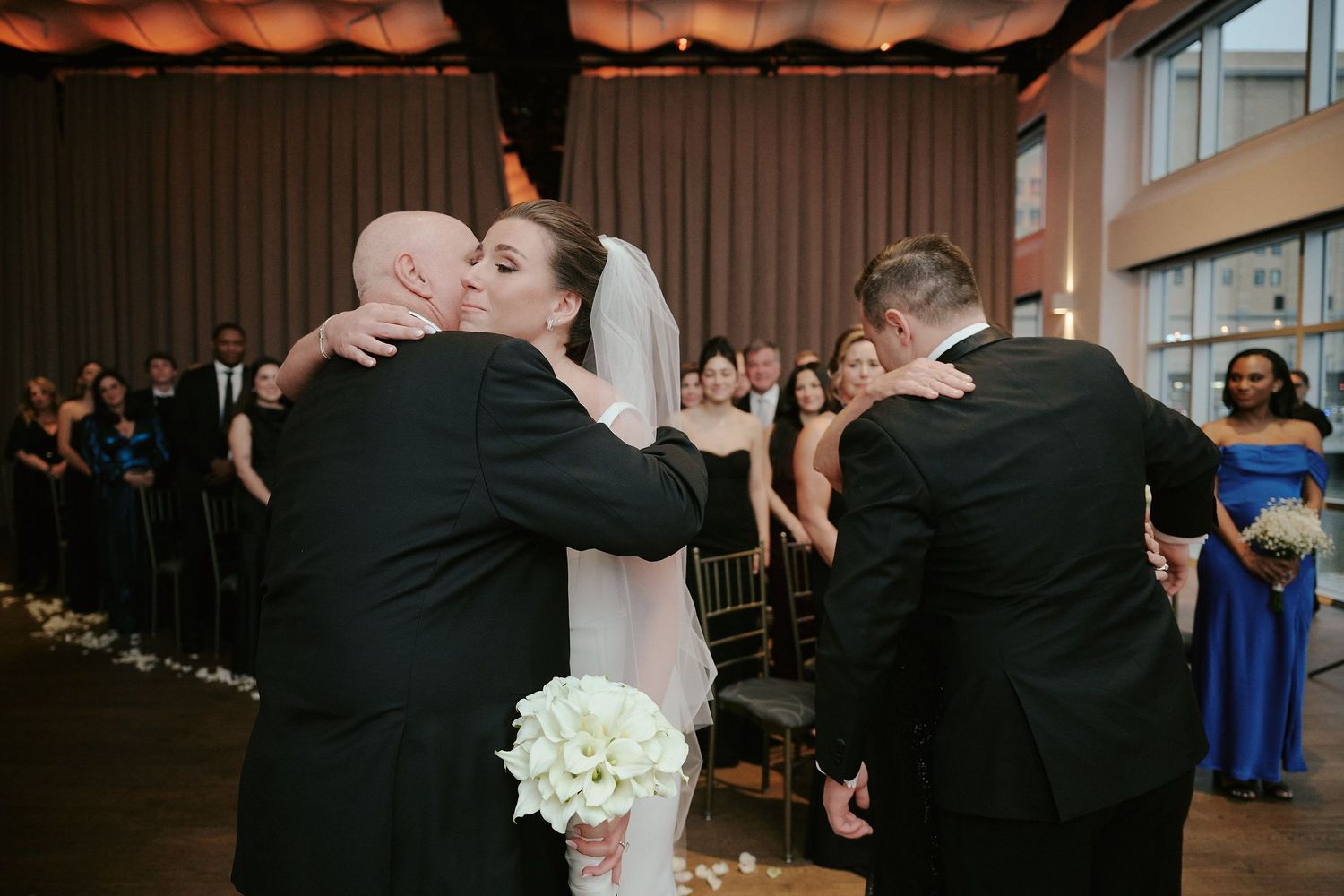 Couples share emotional first dance moment at indoor wedding reception with guests looking on.