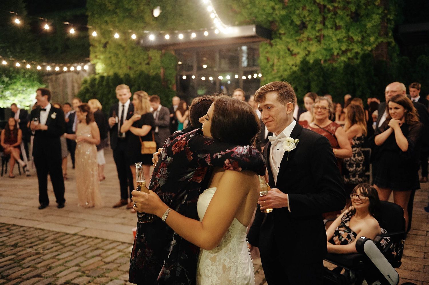 Wedding couple and guests dancing beneath string lights at an outdoor evening reception.