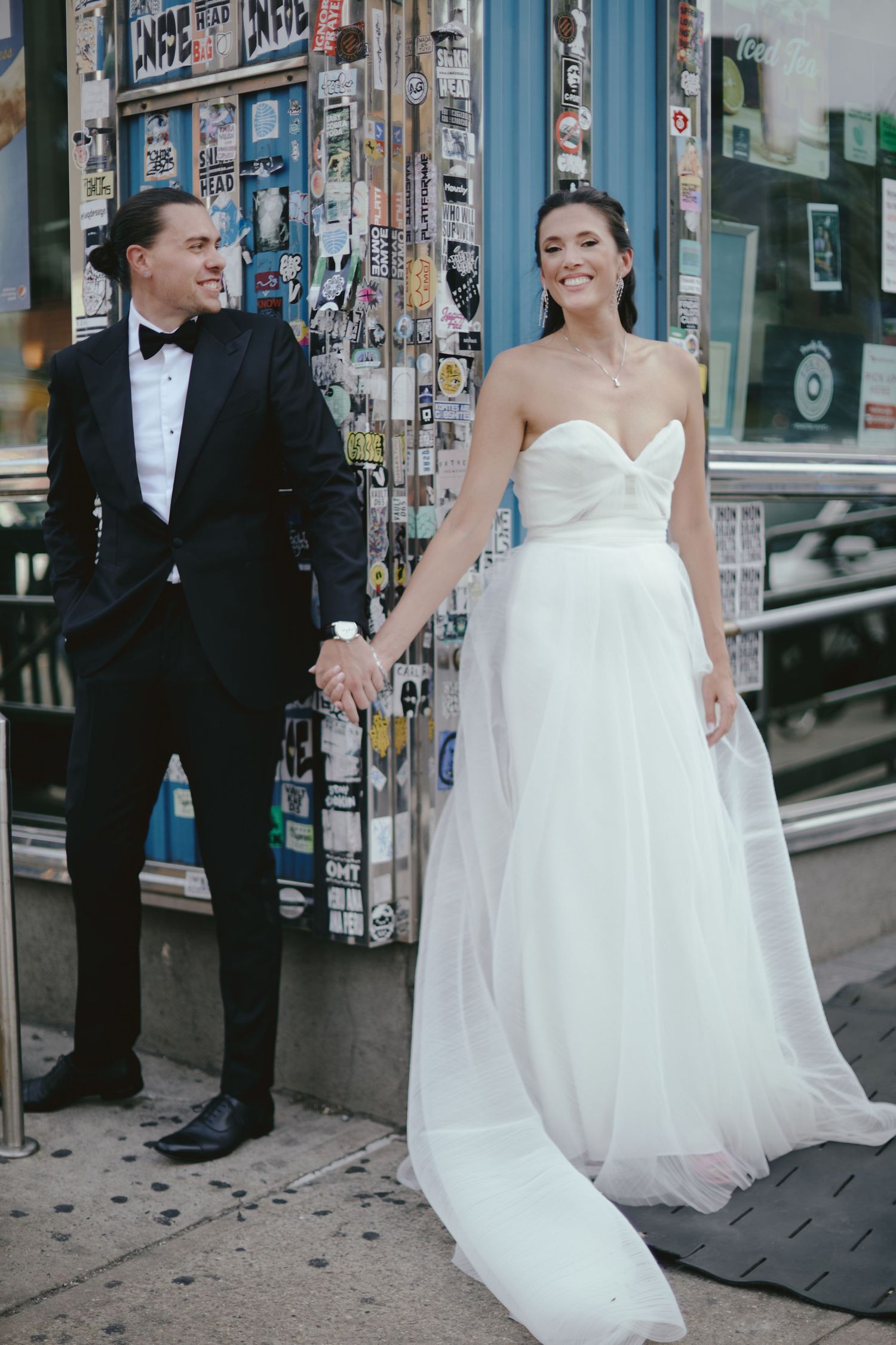 Wedding couple standing together on urban street with posted flyers in background while wearing formal attire.