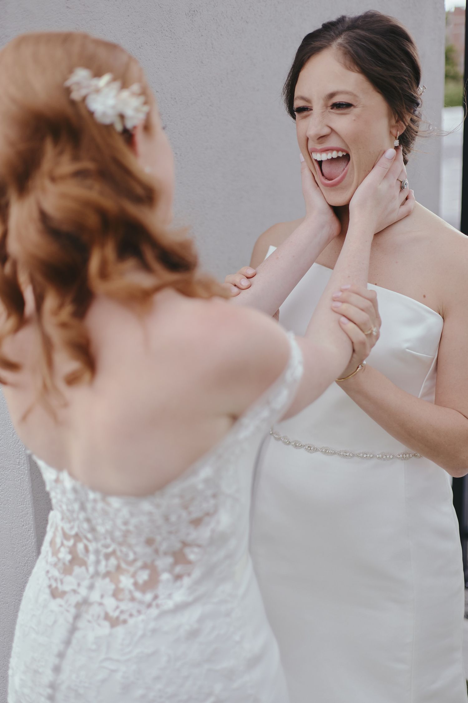 Two brides share a joyful moment of laughter together while wearing elegant white wedding dresses.