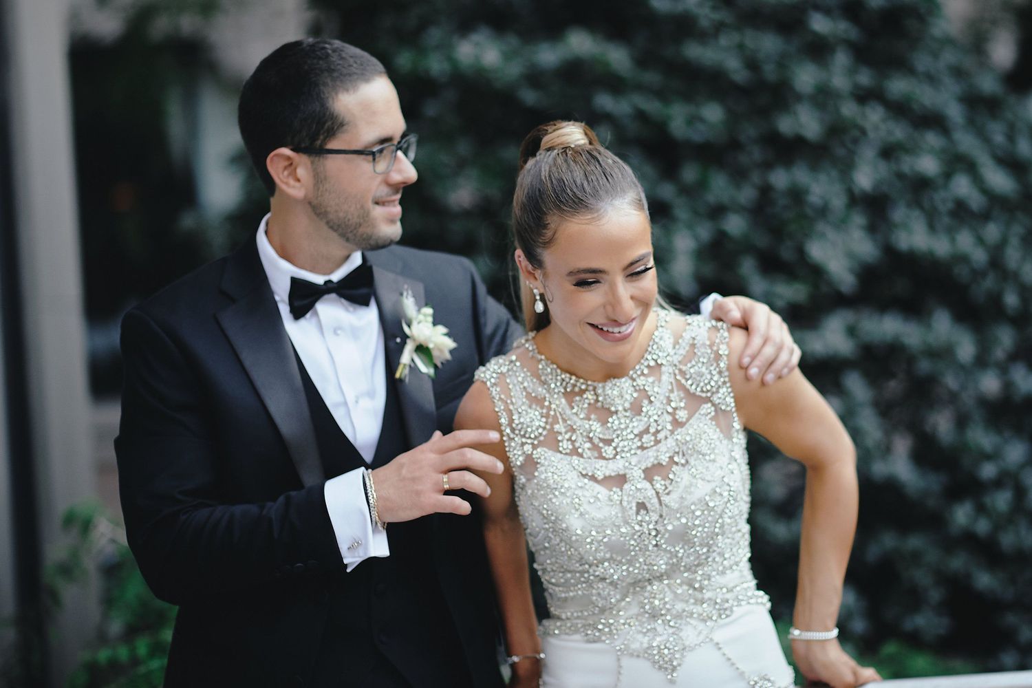 A joyful couple shares a candid moment on their wedding day, with lush greenery in the background.