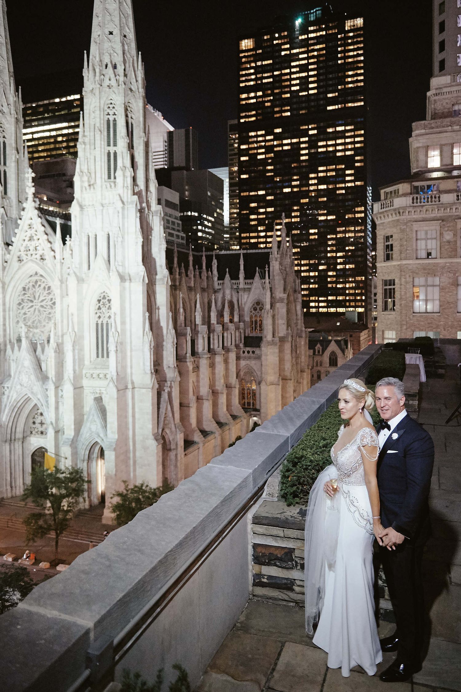 Saint Patrick's Cathedral illuminated at night with skyscrapers in the background creating a dramatic cityscape.