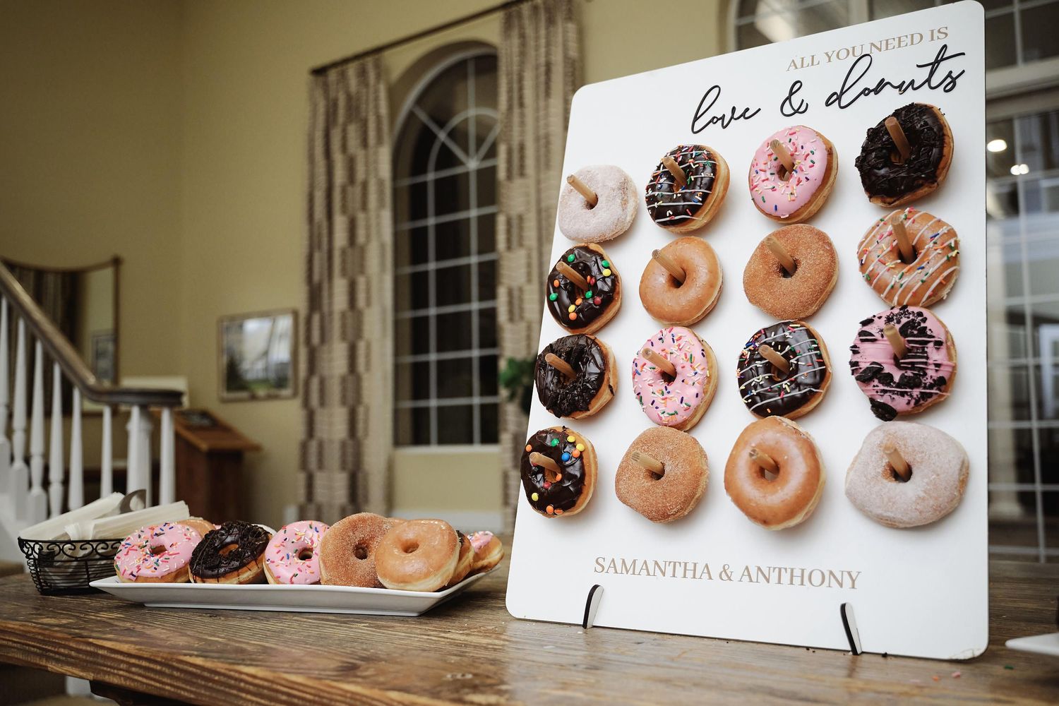 Wedding reception donut wall display with pink and chocolate glazed donuts arranged on a white board with signage.