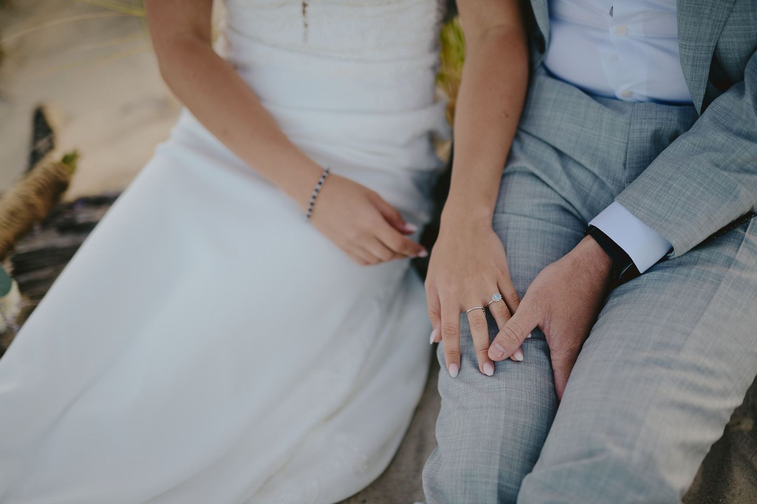 Close up detail of a bride and groom's hands and wedding attire while sitting together.