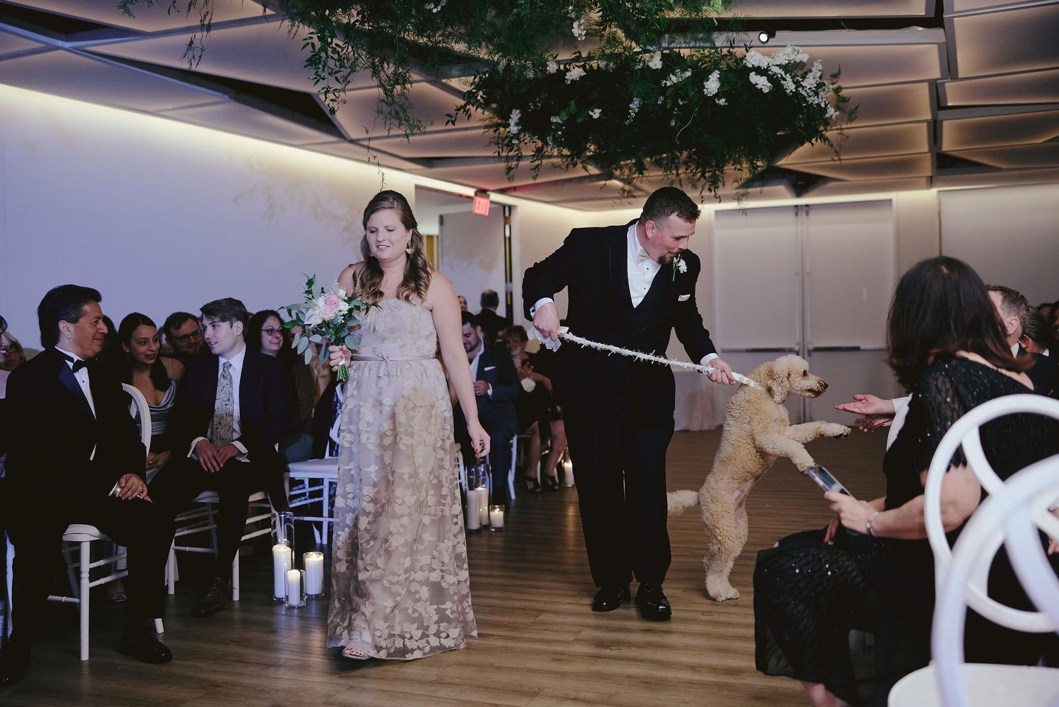Wedding reception guests walking down an indoor aisle at an elegant venue with modern decor and mood lighting.