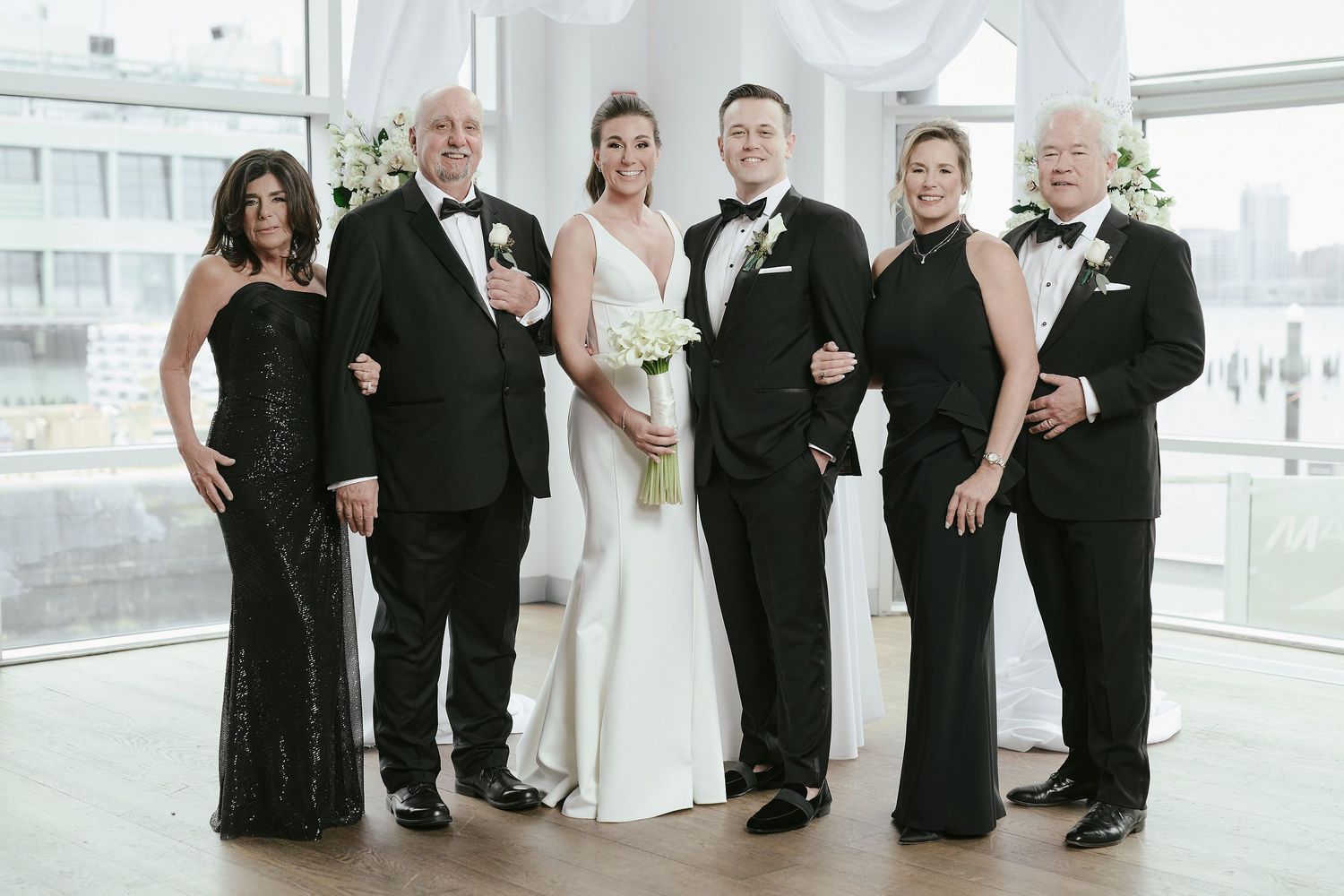 Wedding party in formal black and white attire poses together in a bright modern venue.