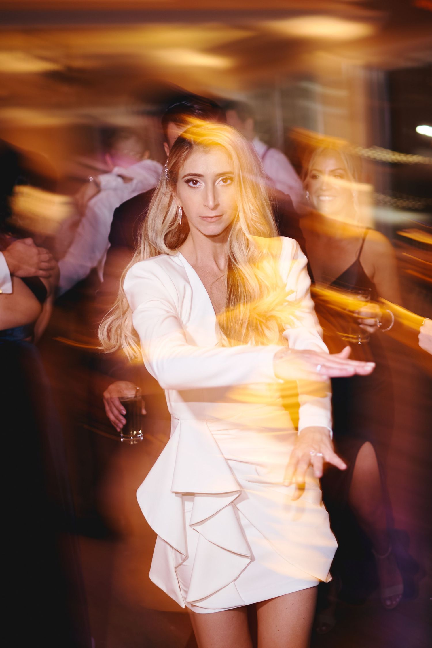 A person in a white ruffled dress dances with motion blur and golden light effects in a nightclub setting.
