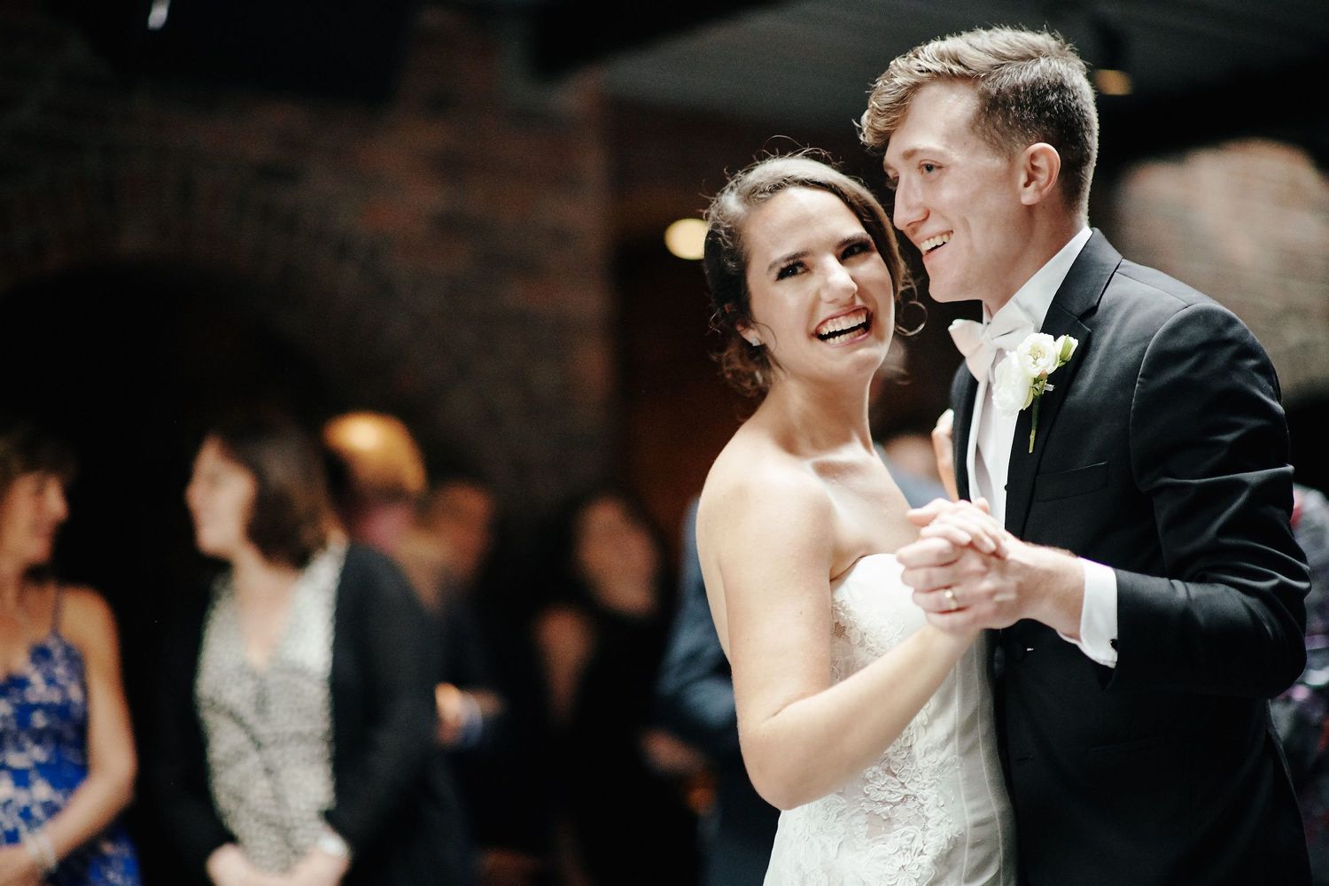 A joyful couple shares their first dance at a wedding reception in a dimly lit venue.