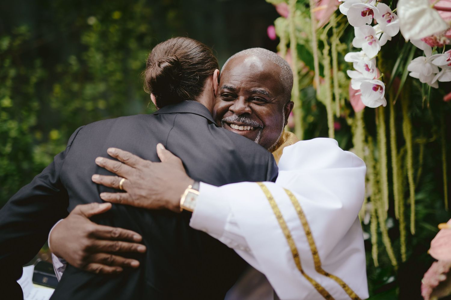Two people share a warm embrace at an outdoor celebration with white orchids in the background.