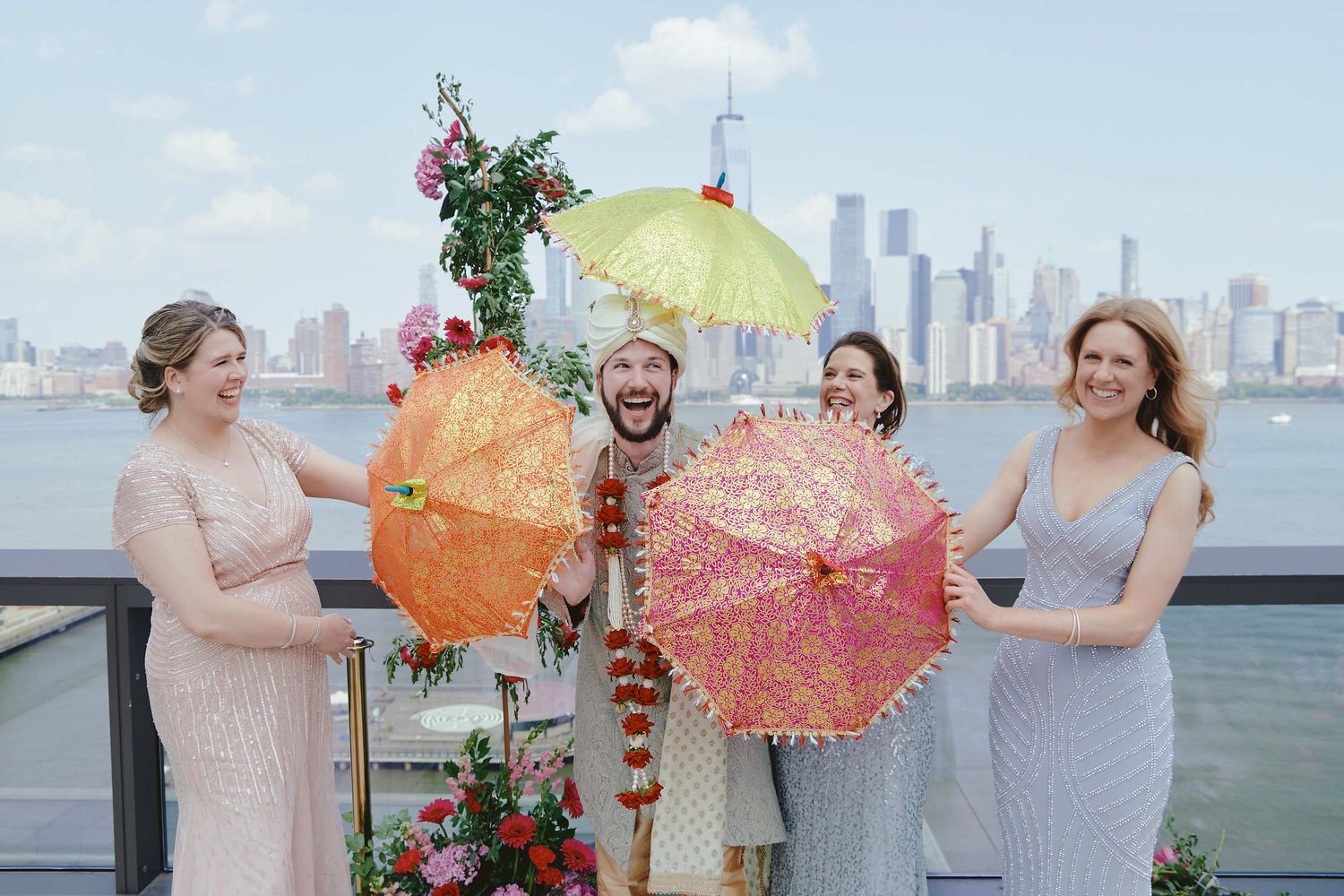 Group of friends pose with colorful parasols against city skyline backdrop at outdoor celebration venue.