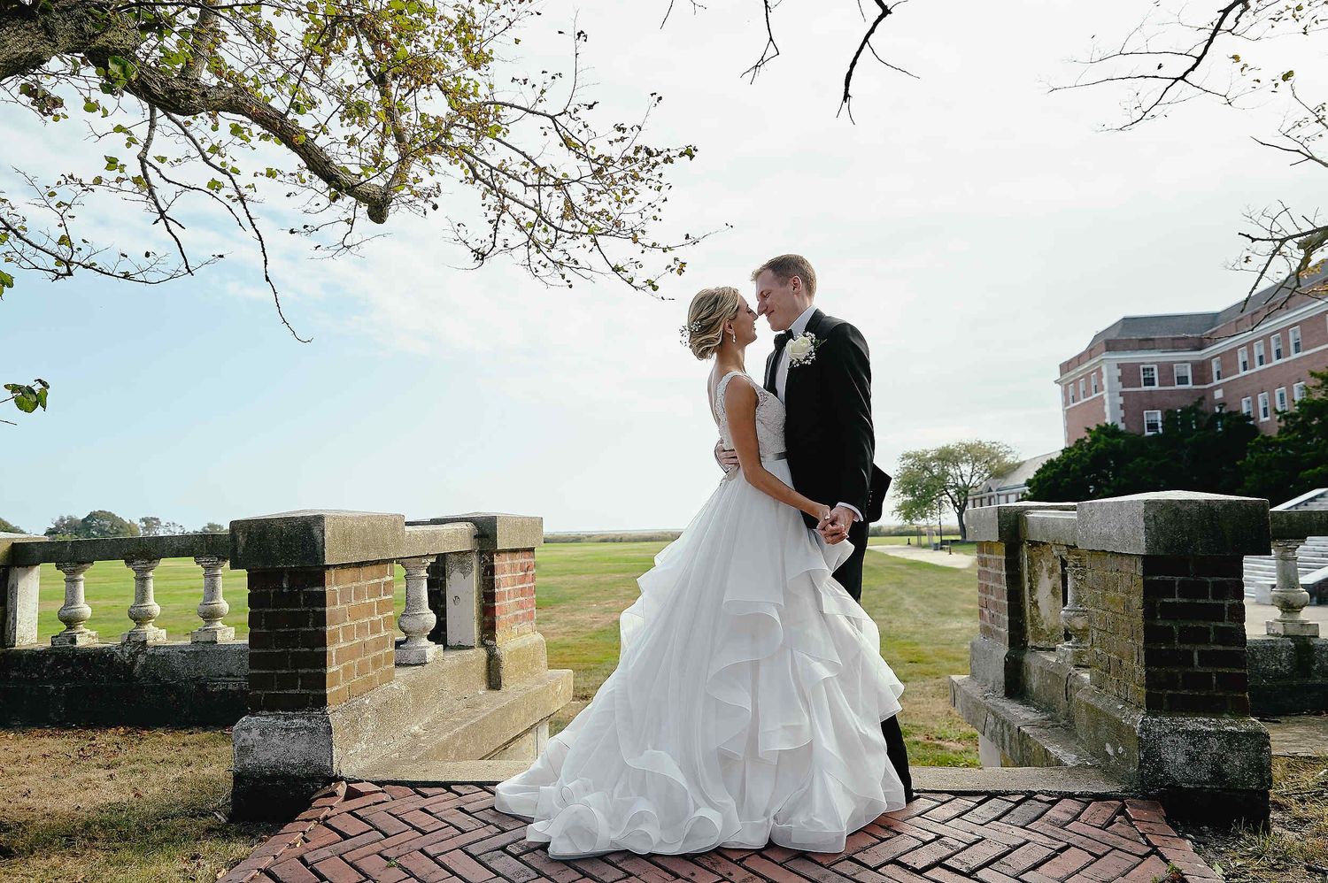 A bride and groom share an intimate moment on a brick path surrounded by stone columns and greenery.