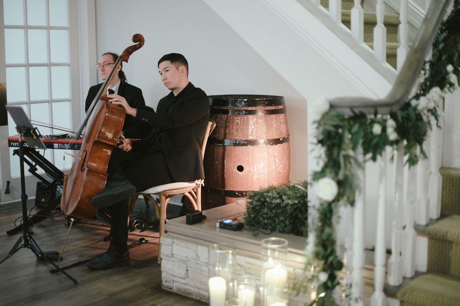 Musicians perform at an indoor wedding venue with upright bass and piano near a white staircase.