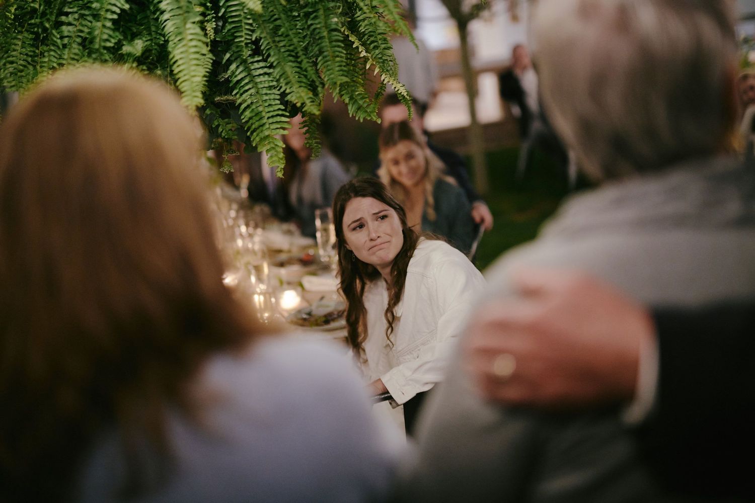 Guest sits at an intimate candlelit table with greenery hanging overhead during an indoor wedding reception.