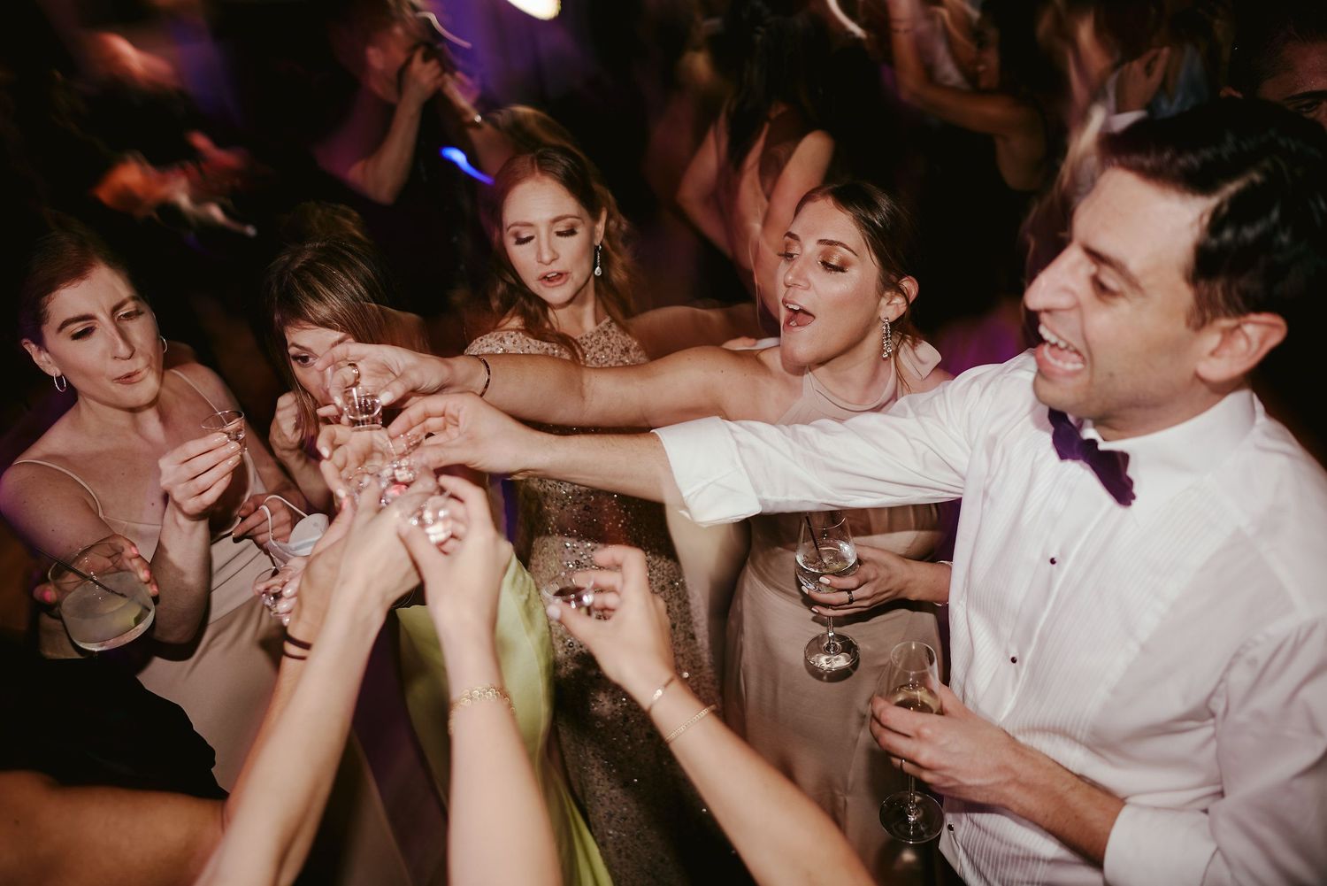A lively wedding celebration with people reaching in to toast and clink their glasses together at a party.