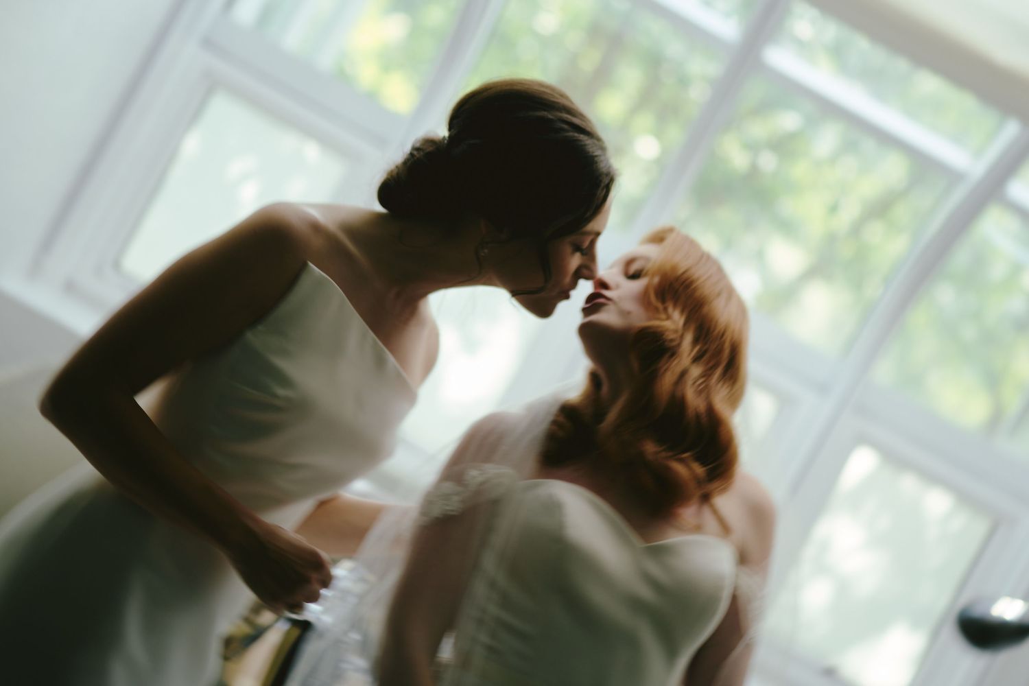 Two people share a romantic moment in front of a bright window, creating a dreamy silhouette effect.