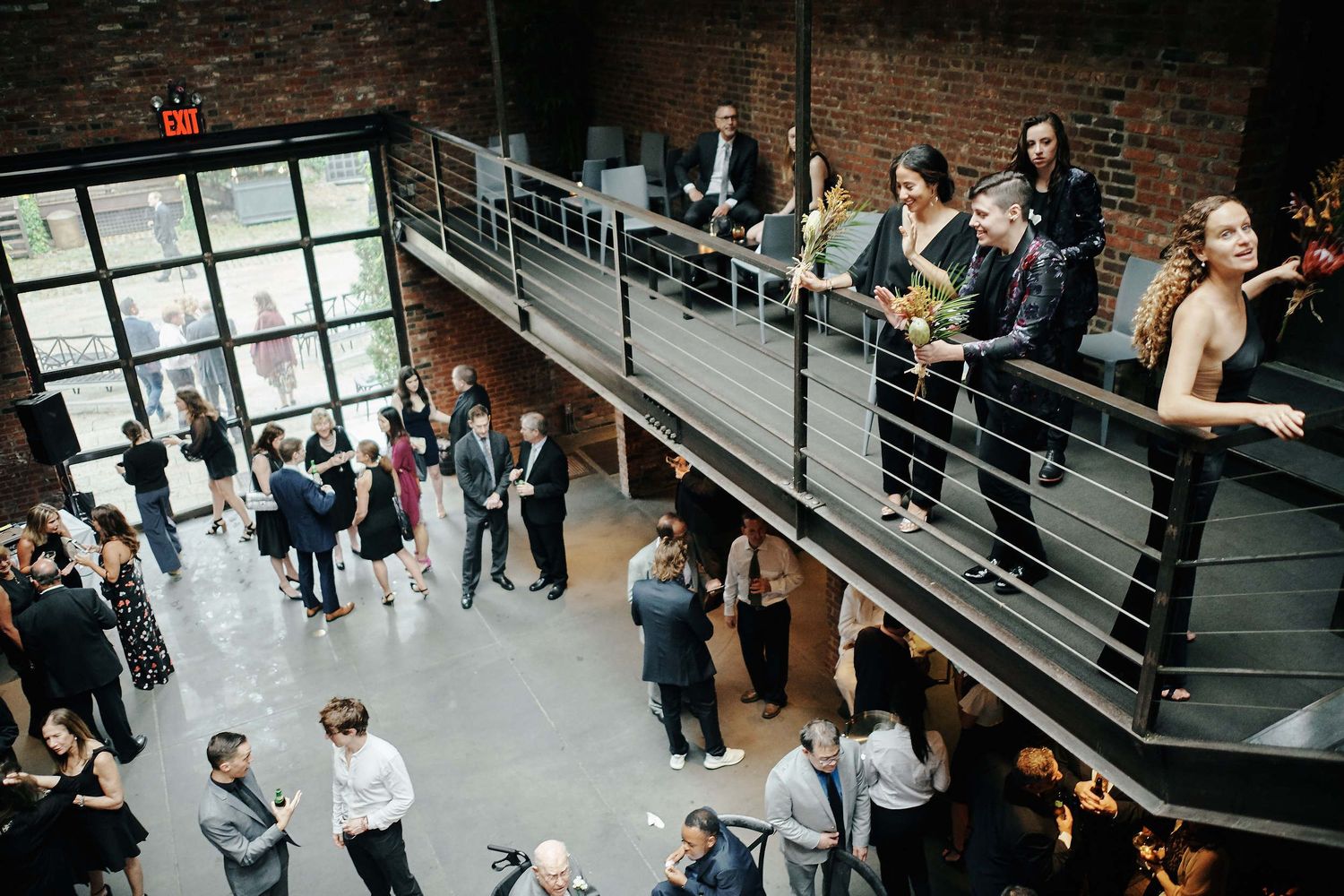 Wedding guests mingle and socialize on a modern industrial staircase in a brick-walled venue.