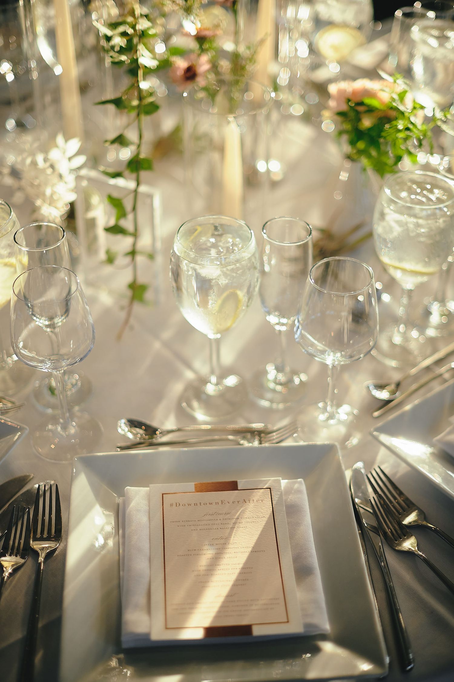 An elegant wedding table setting with wine glasses, place settings and floral decorations in natural light.