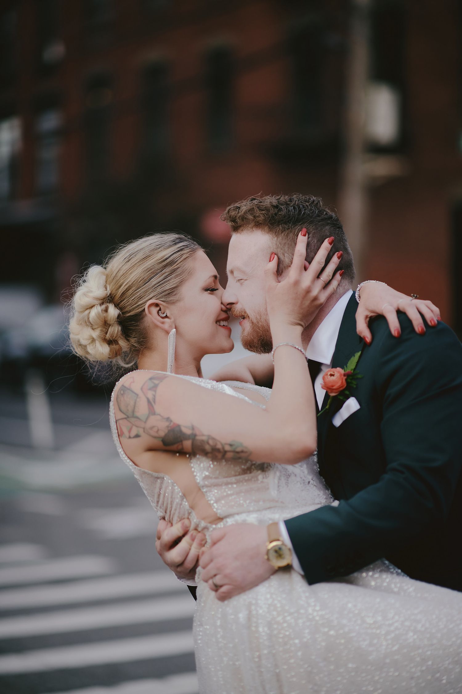 A romantic wedding moment captured on a city street with the couple sharing an intimate kiss against a brick building backdrop.