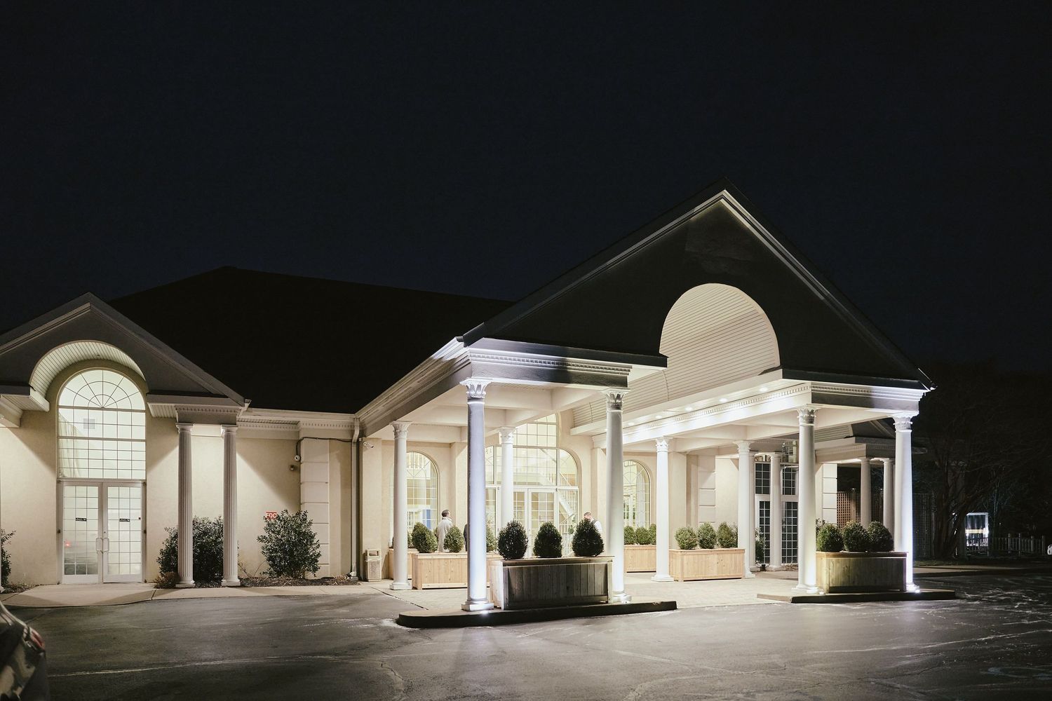 Elegant entrance of a white funeral home illuminated at night with columns and arched windows.