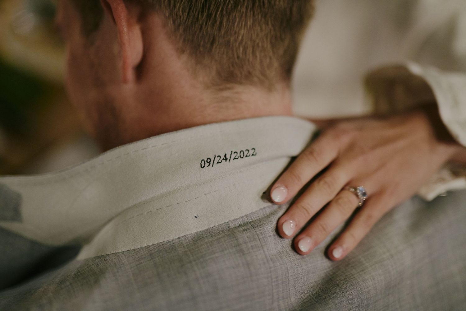 Close-up view of an engagement ring on a hand resting on someone's shoulder with a date stamp visible.
