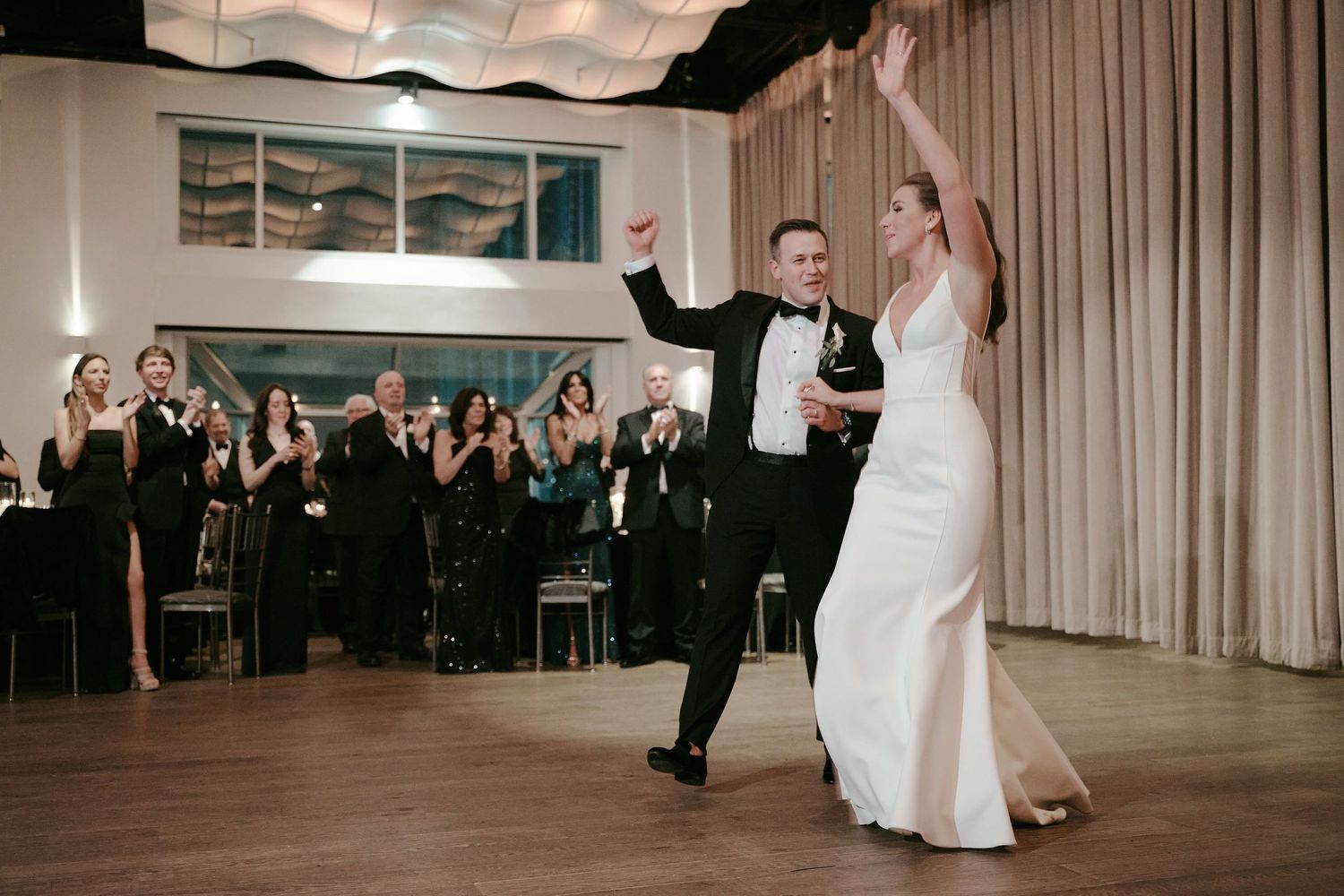 A couple in formal attire dancing gracefully across a ballroom floor while guests watch from their tables in the background.