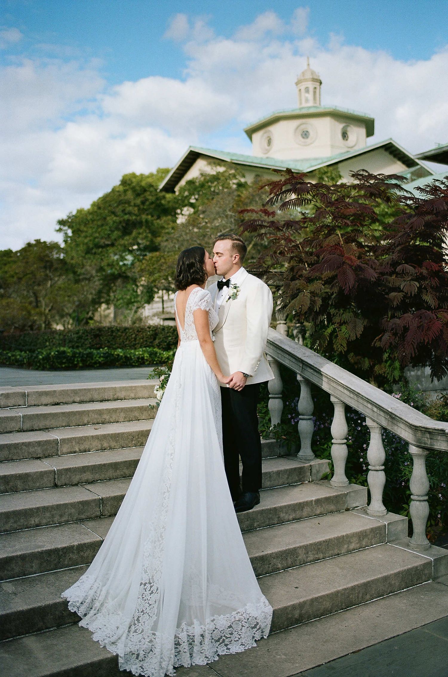 A romantic wedding photograph on grand stone steps with ornate balustrade and a domed building in the background.