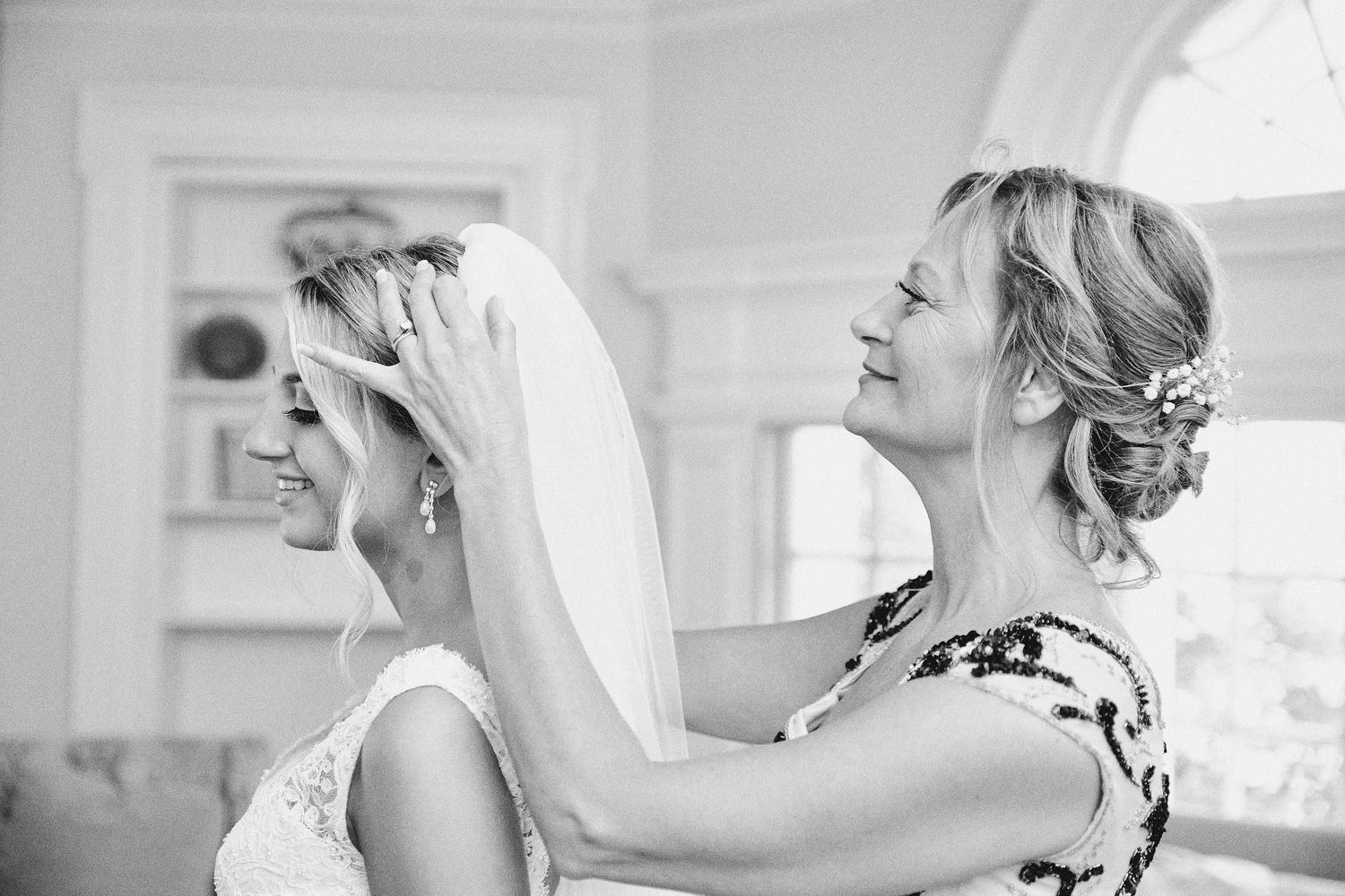 A bride has her veil adjusted in an elegant black and white photo during wedding preparations.