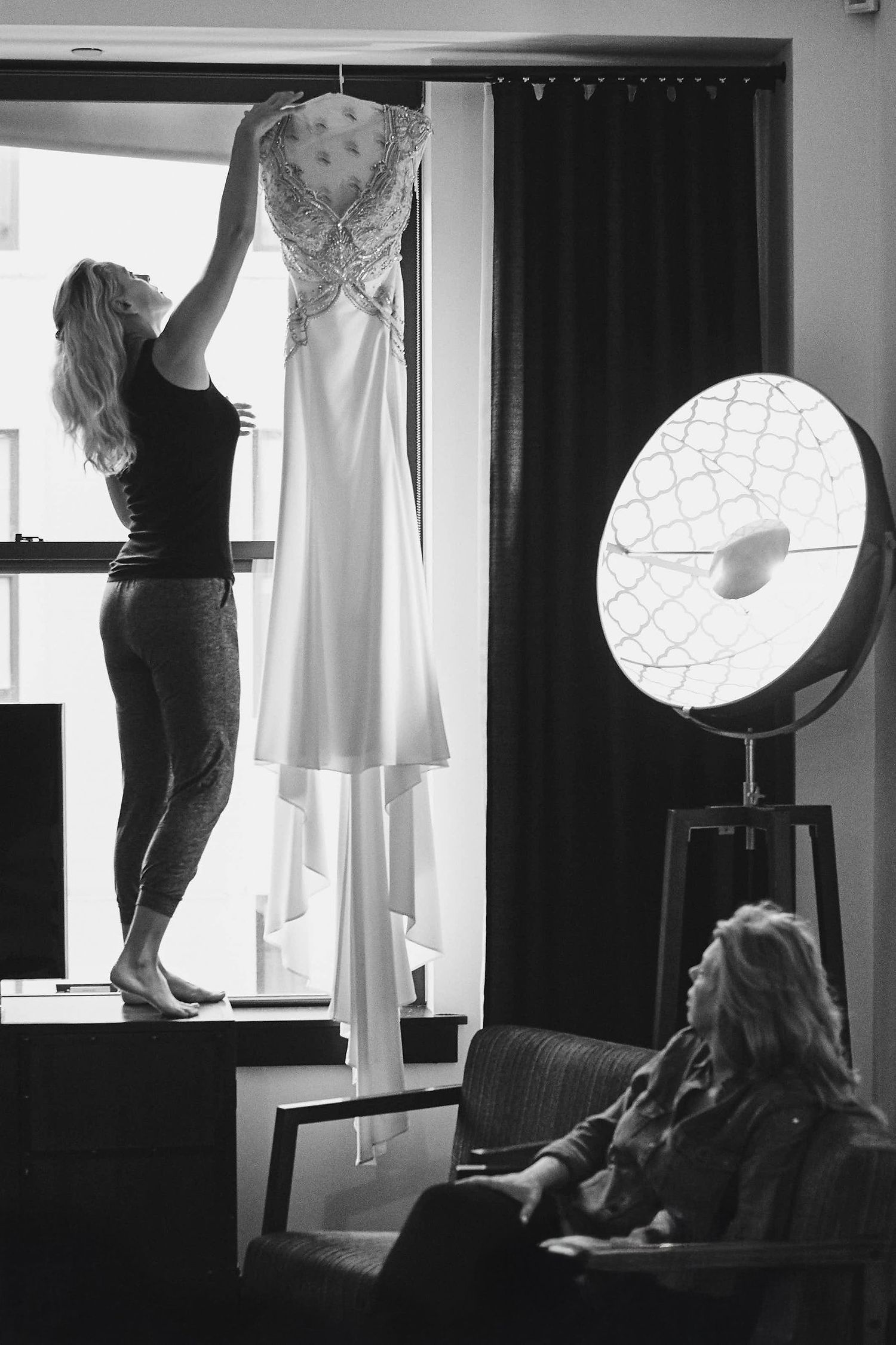 Monochromatic image of wedding dress preparation with large lighting equipment in background.