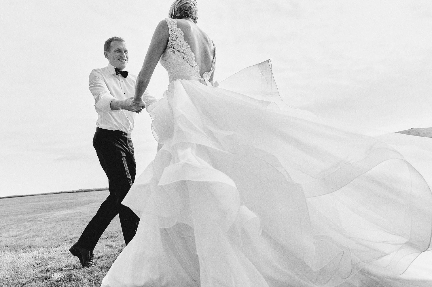 Black and white photo of couple dancing outdoors with bride's dress flowing in the wind.