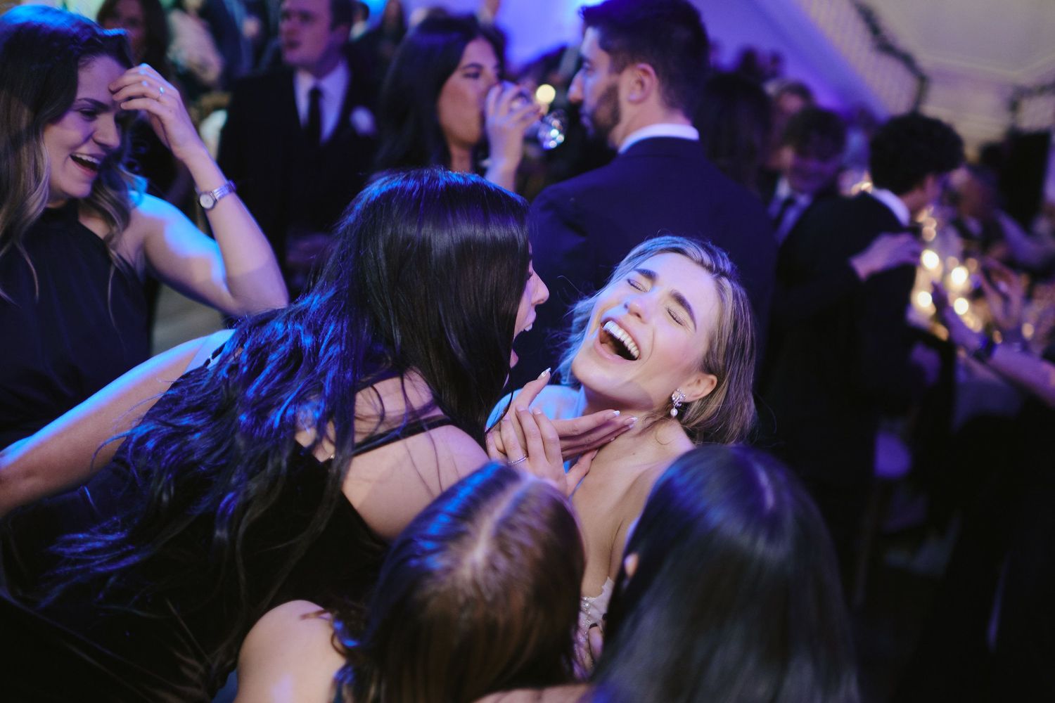 Joyful partygoers share a candid laughing moment on a crowded dance floor at an evening celebration.
