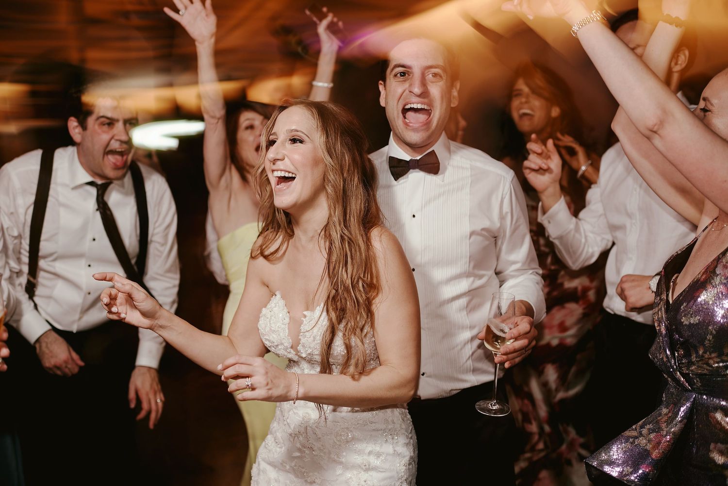 Wedding reception guests dance joyfully together on the dance floor in formal attire at an indoor venue.