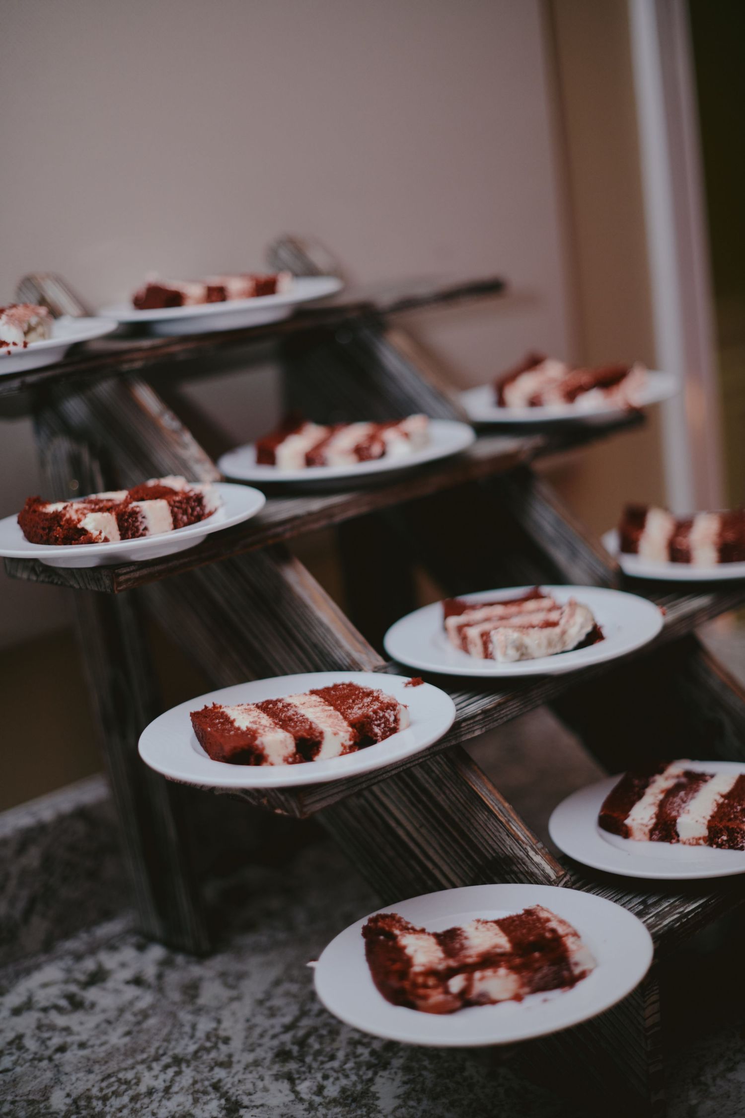 Several slices of chocolate cake with white frosting stripes arranged on white plates on a dark textured surface.