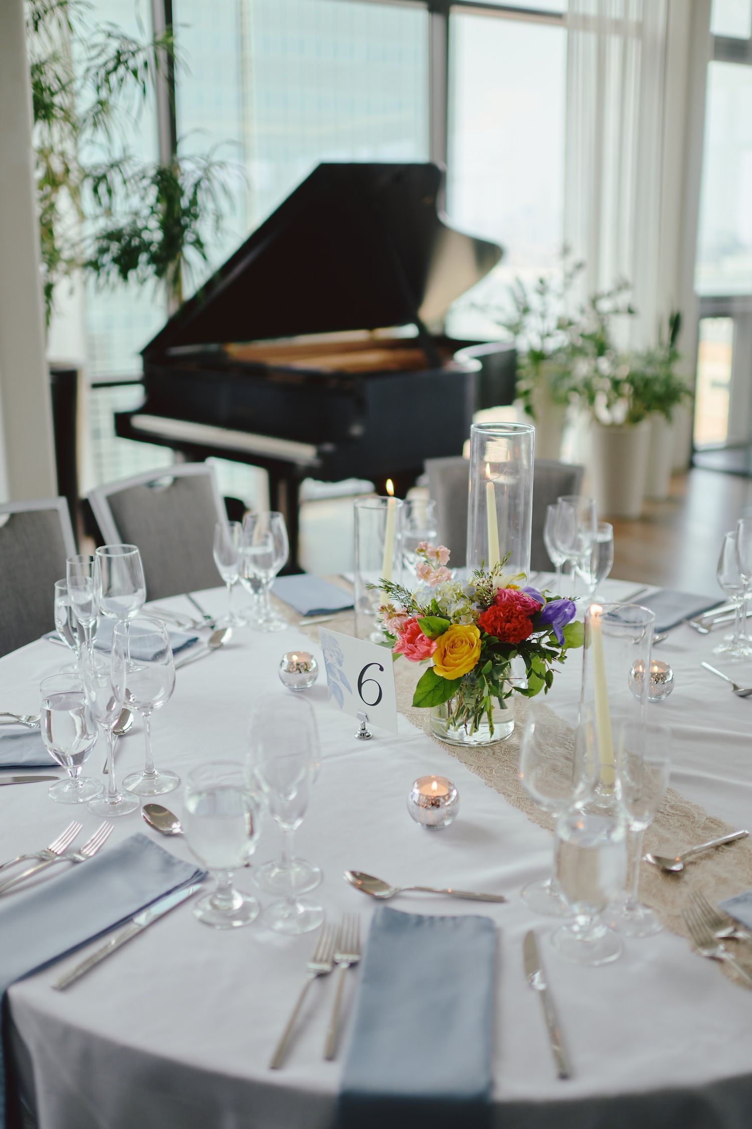 Elegant wedding reception table setting with grand piano and colorful floral centerpiece.