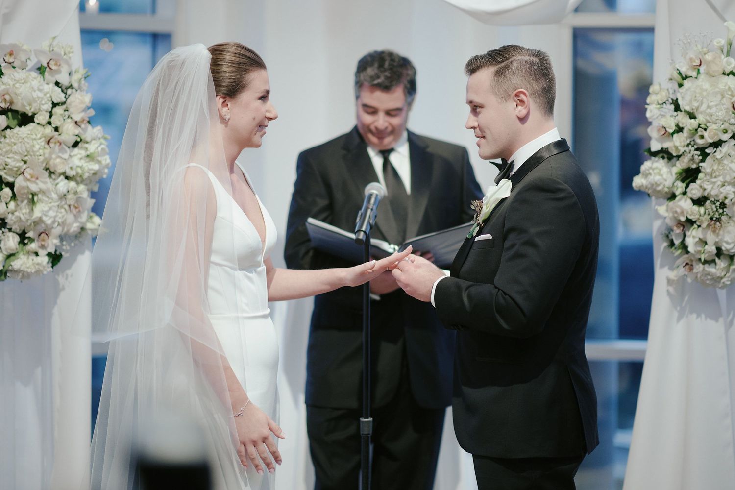 An elegant wedding ceremony in a church with white floral arrangements and decorations flanking the altar.