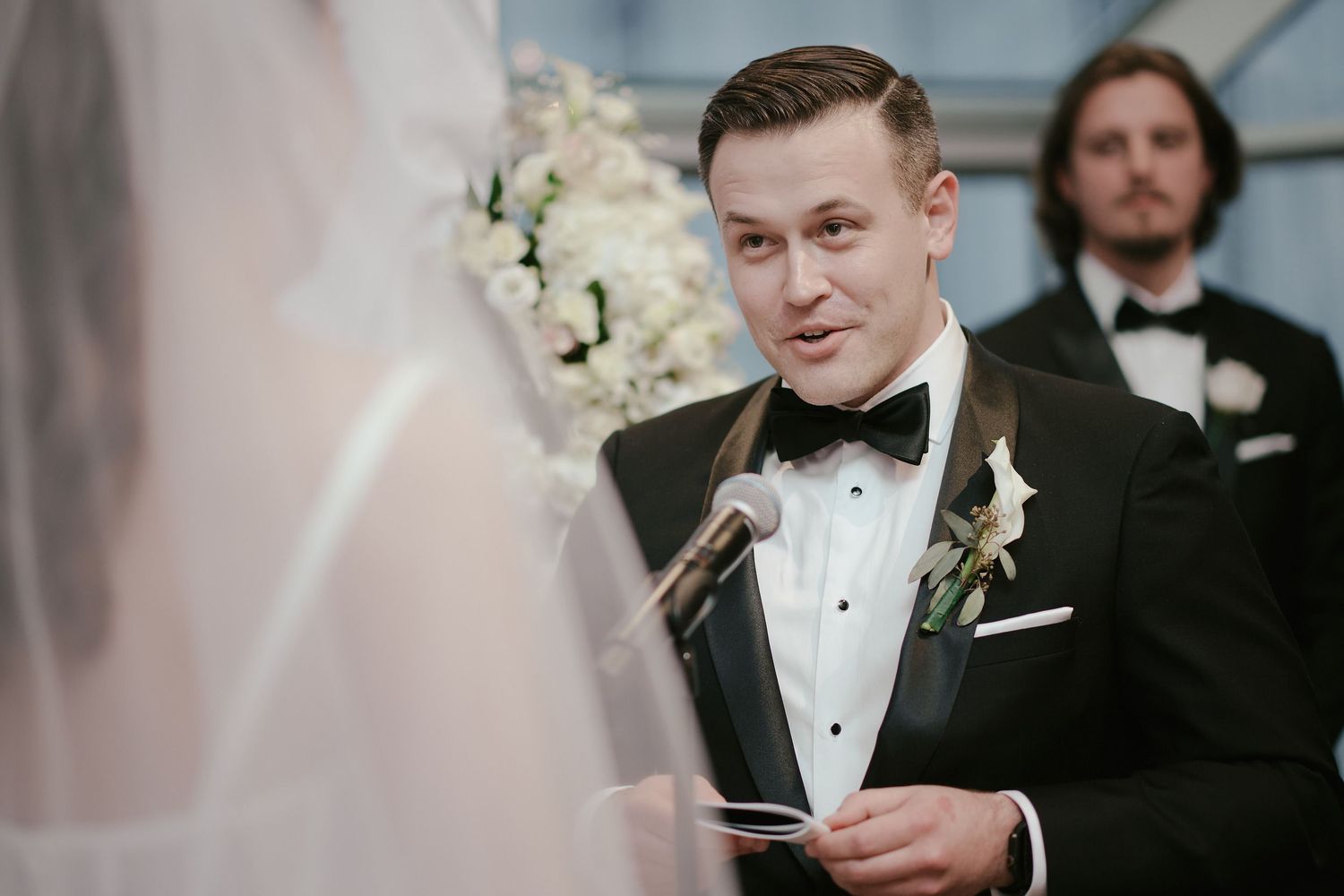 Wedding ceremony moment showing a formal exchange of vows at an indoor venue with floral decorations.