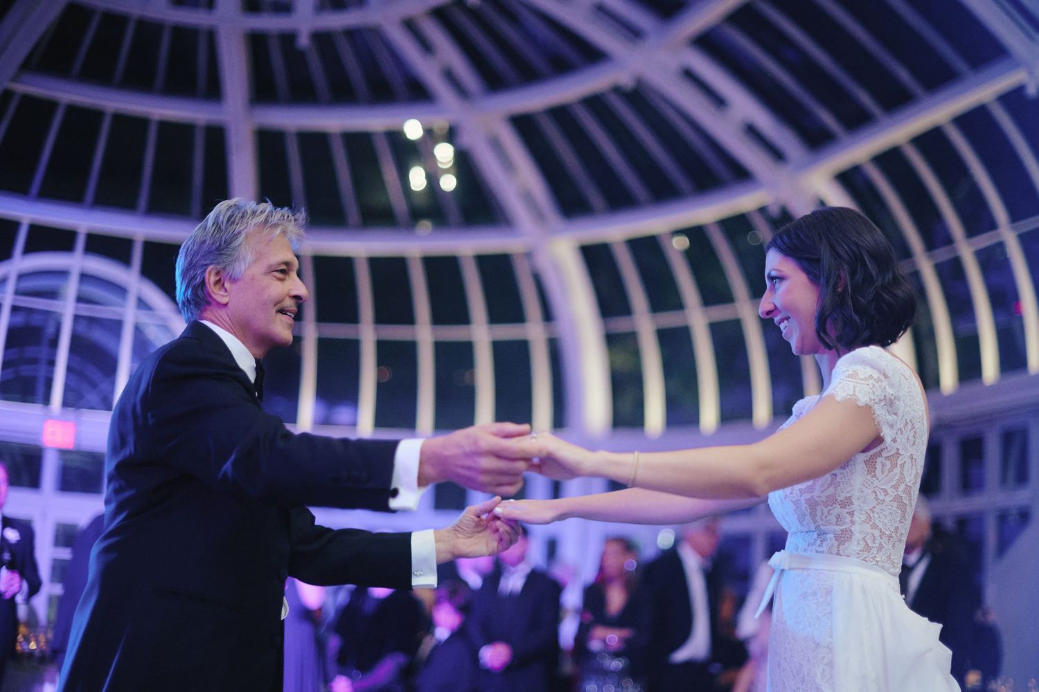 Couple dancing together beneath illuminated glass dome ceiling at elegant evening celebration.
