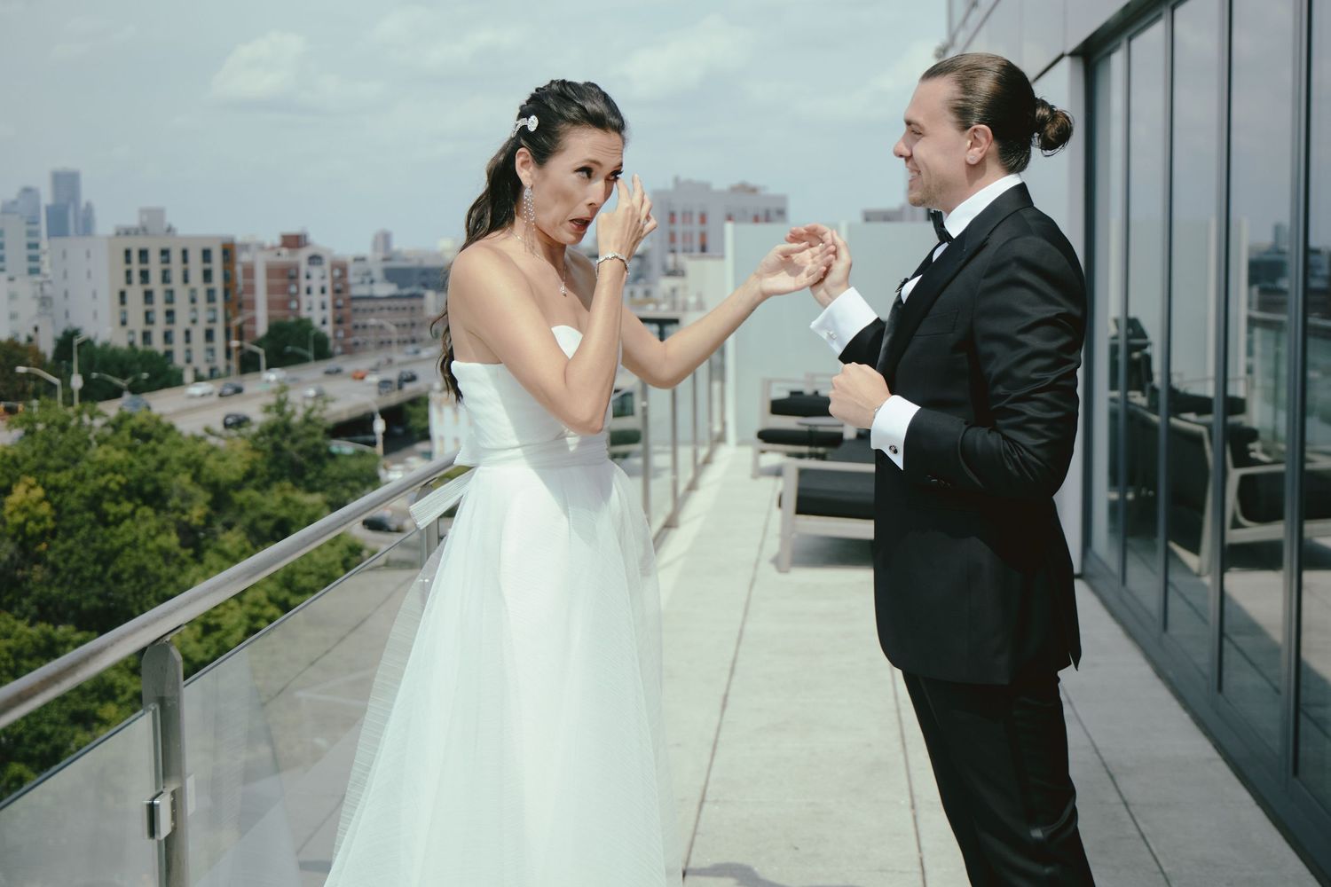 A person in a white wedding dress and someone in a tuxedo share a playful moment on a rooftop terrace in the city.