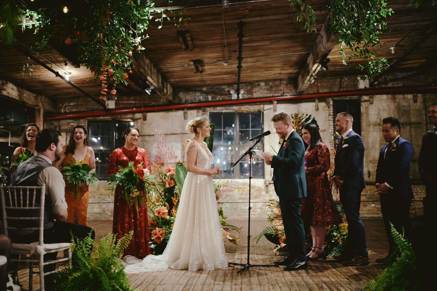 Rustic indoor wedding ceremony with greenery decorations and string lights in an intimate wooden venue setting.