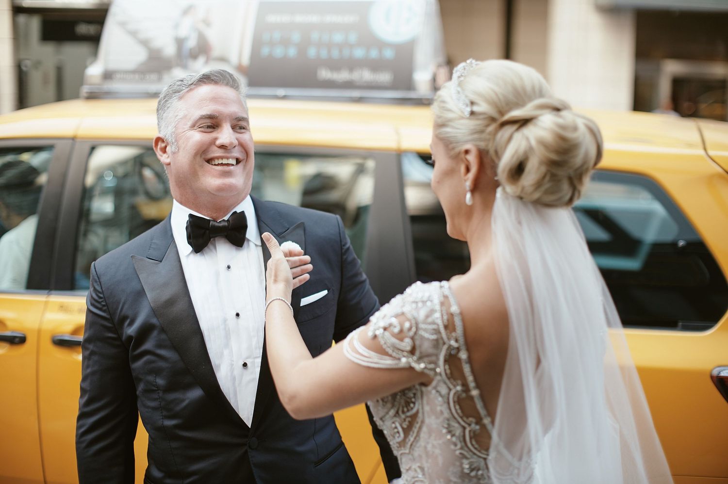 Newlyweds share a joyful moment on their wedding day in front of a yellow taxi cab in the city.