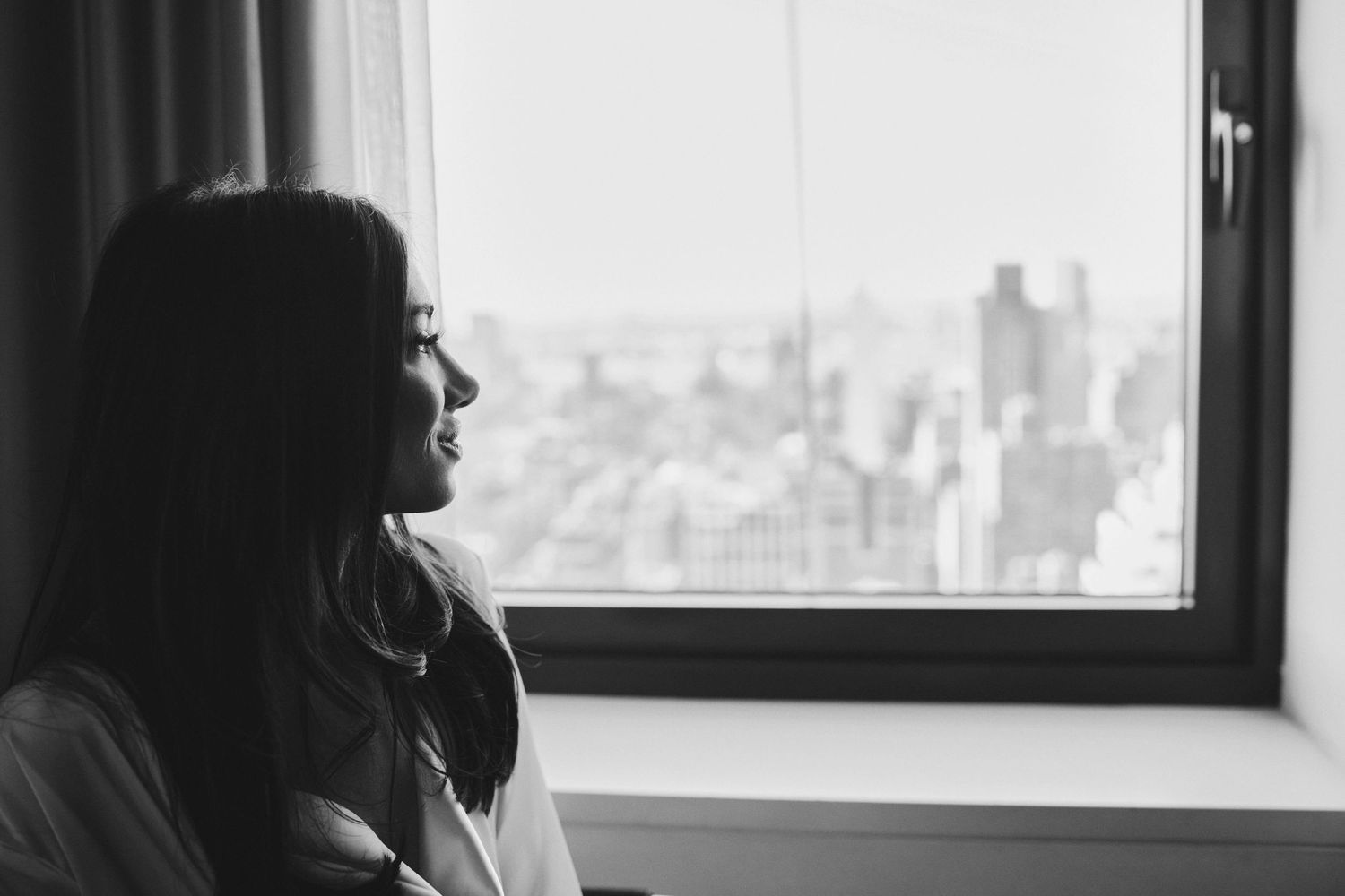 Black and white silhouette gazing through window at distant city skyline in contemplative moment.