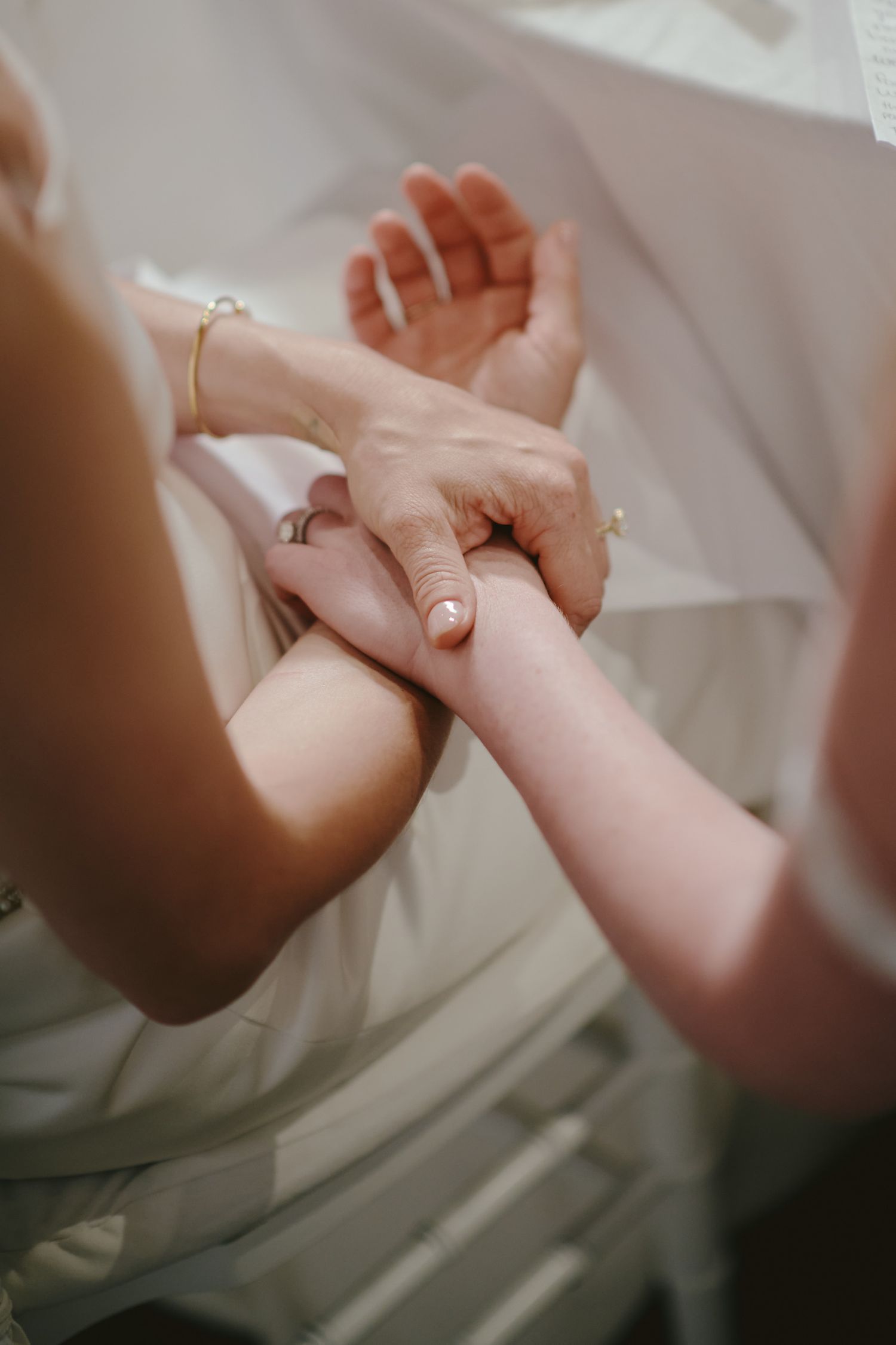 Two hands gently clasped together against white fabric, with one wearing a delicate wedding ring.