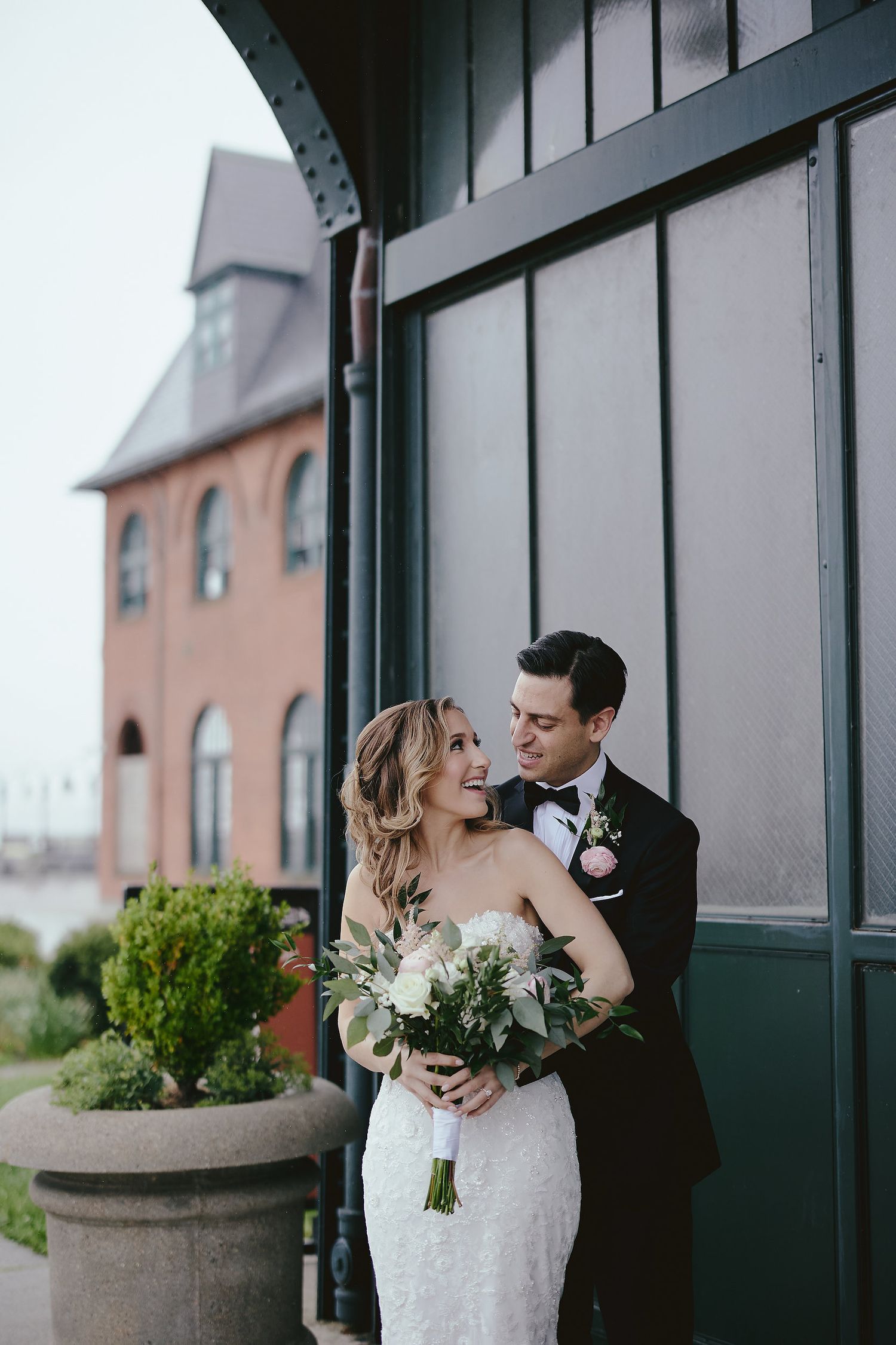 Newlywed couple shares intimate moment outside historic brick church with dark green doors and grey overcast sky.