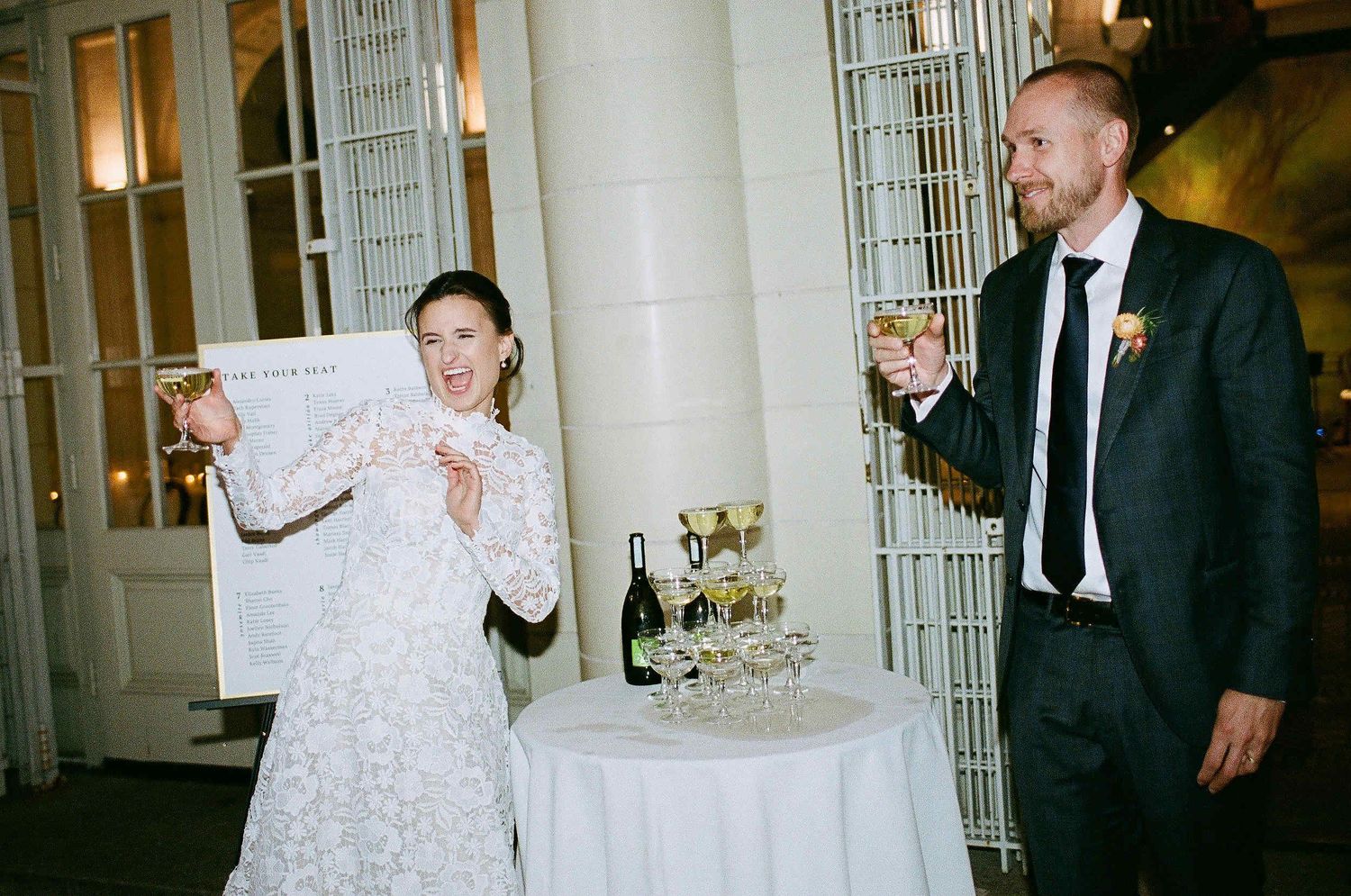 A couple raises their glasses in celebration by an elegant cake table during their wedding reception.