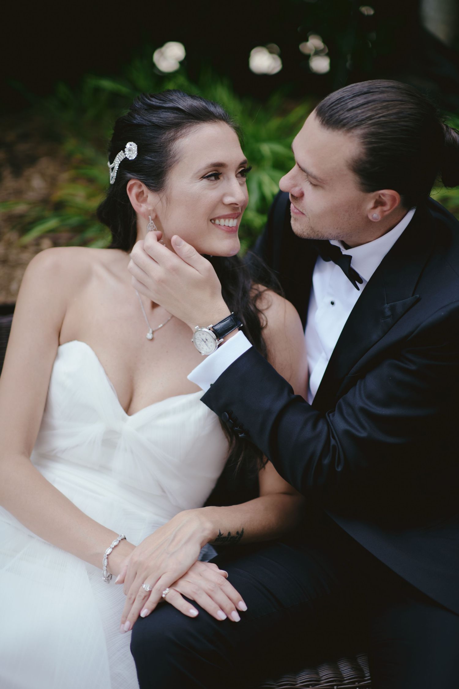 A romantic moment between newlyweds in formal wedding attire with lush greenery in the background.