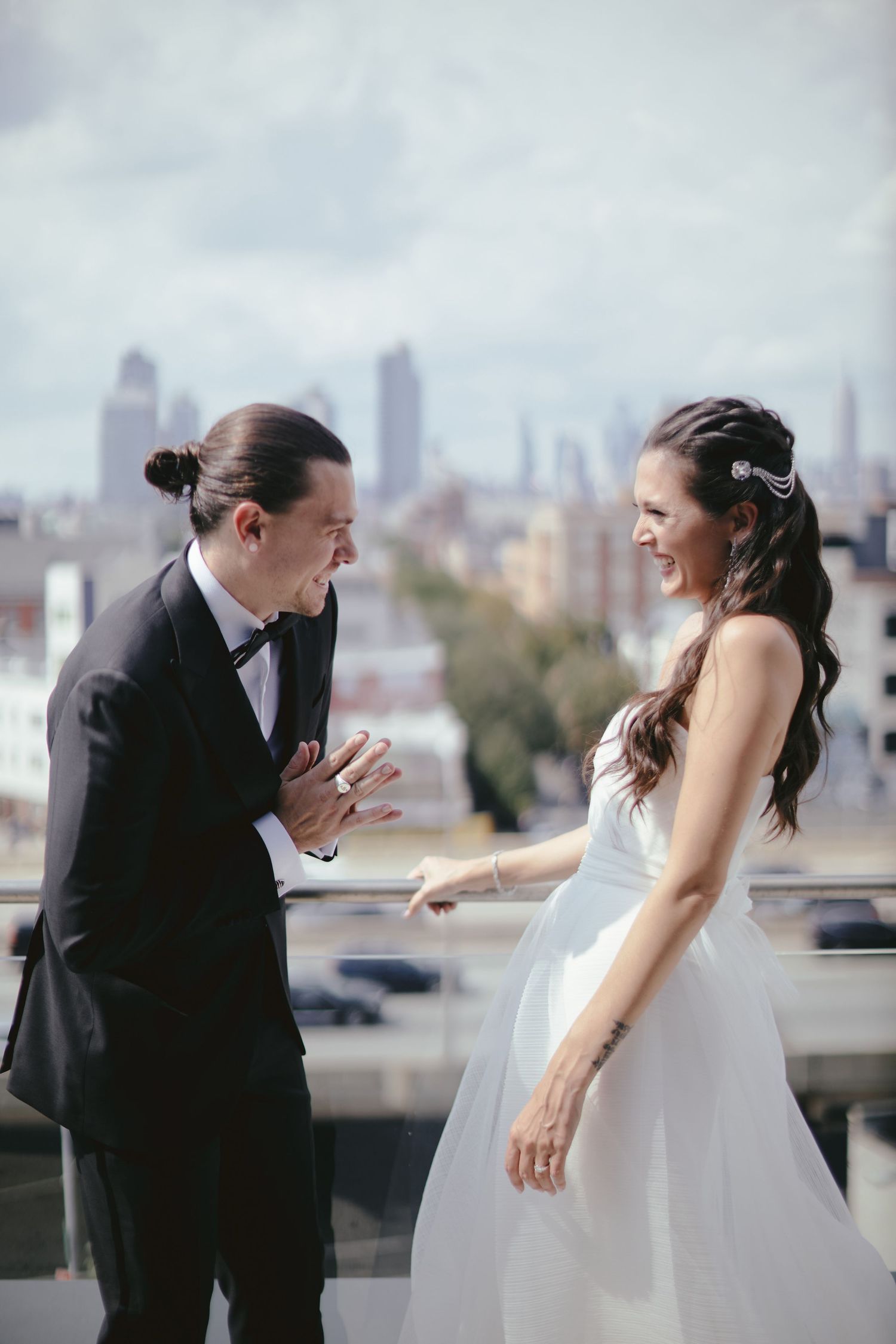 A couple sharing a joyful moment in their wedding attire with city skyline in the background.