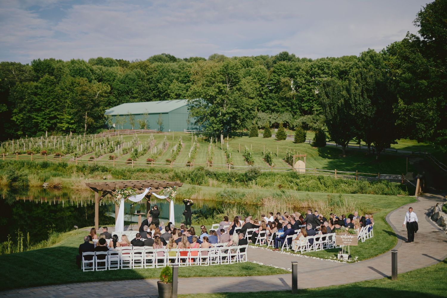 An outdoor wedding ceremony setup with white chairs and decorative arch overlooking a scenic hillside venue with green barn.