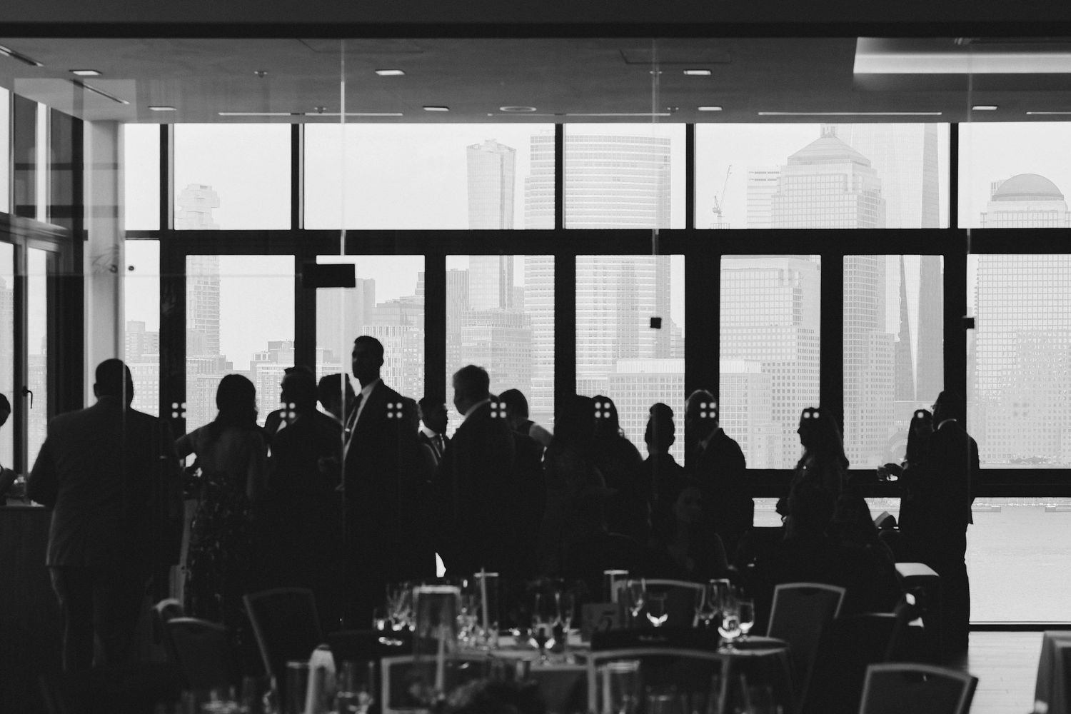 Dark silhouettes of people gathered by large windows in a modern restaurant or conference space.