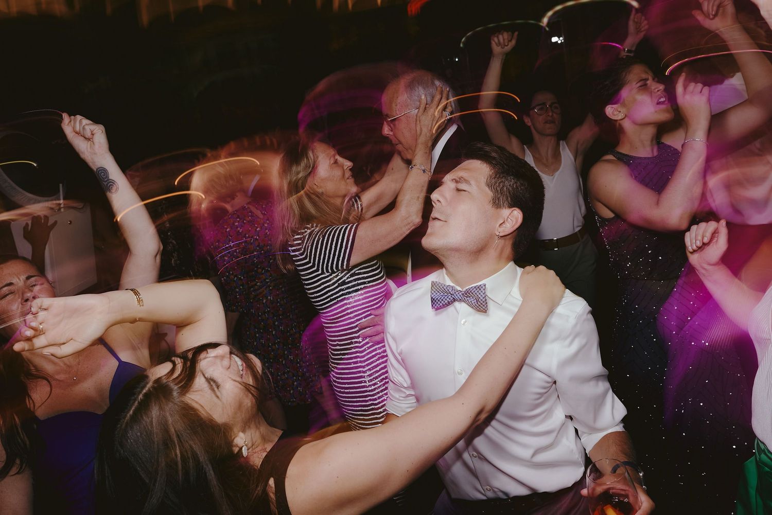 A crowd of dancers moving energetically on a dimly lit dance floor with purple lighting effects.